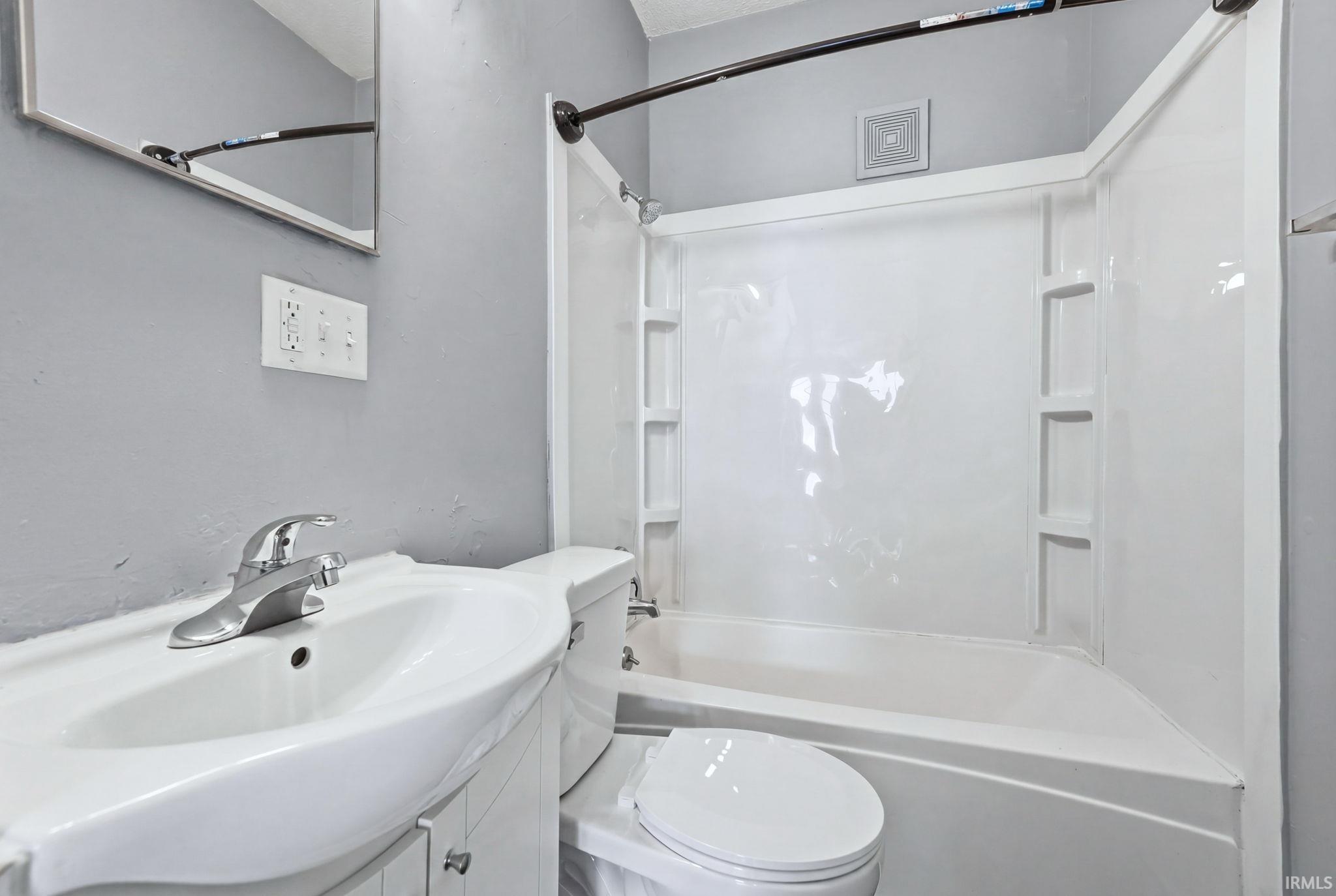 Bathroom featuring a white vanity with an integrated sink, a chrome faucet, a white toilet, and a white bathtub with a shower surround