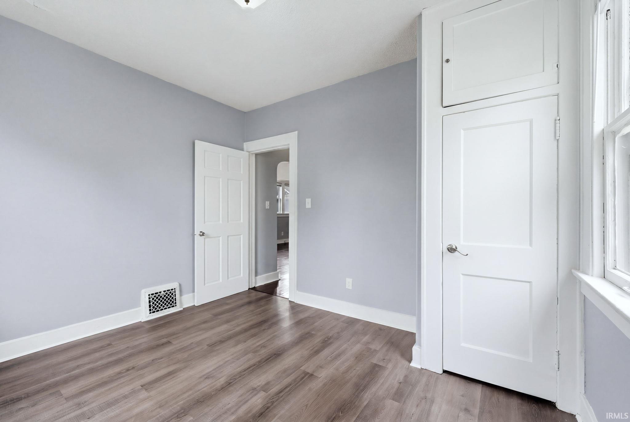 Interior room featuring wood-finish flooring, light purple wall paint, white trim, and a white paneled door