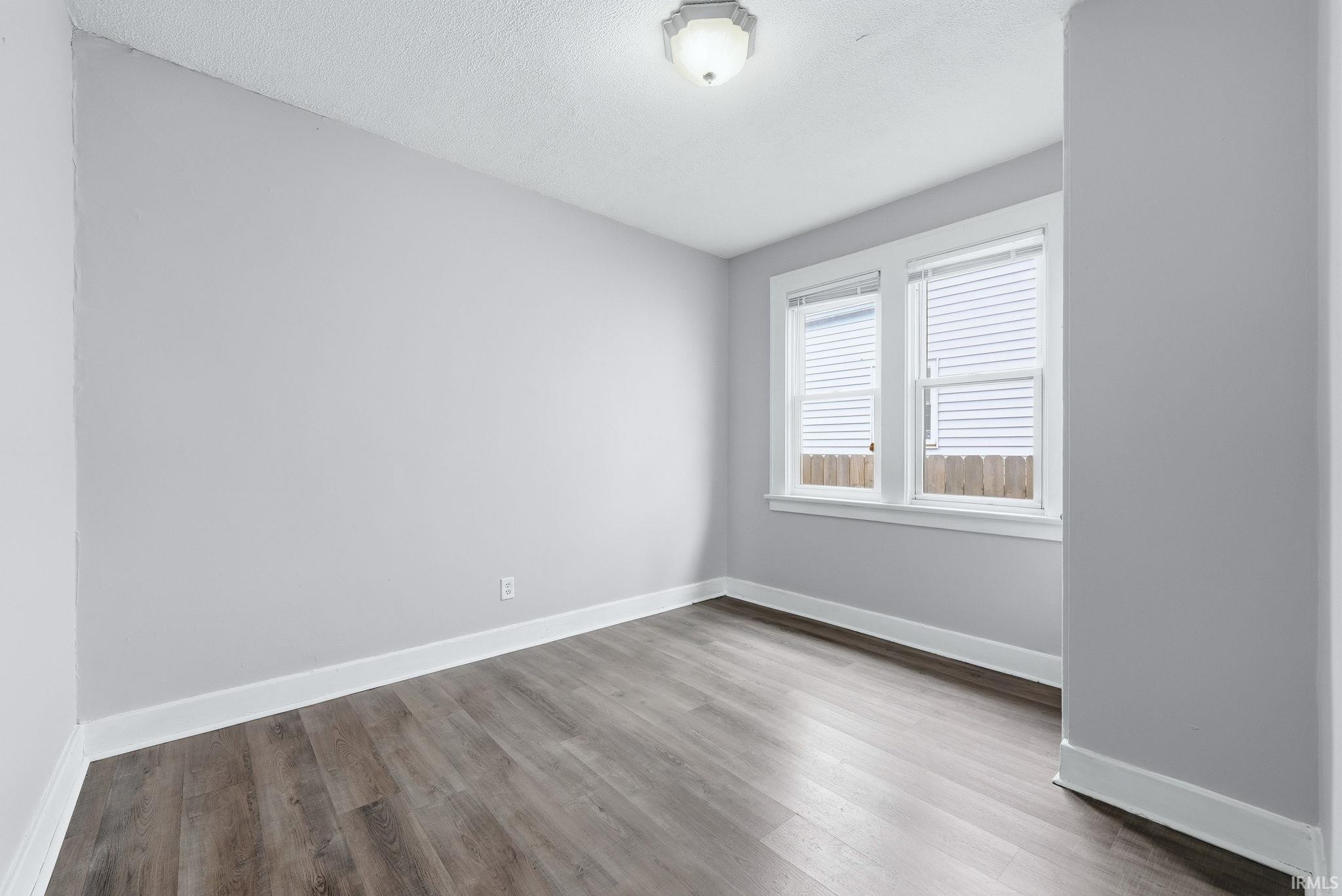 Spacious room featuring wood-finish flooring, light gray walls, white trim, and two double-hung windows with blinds