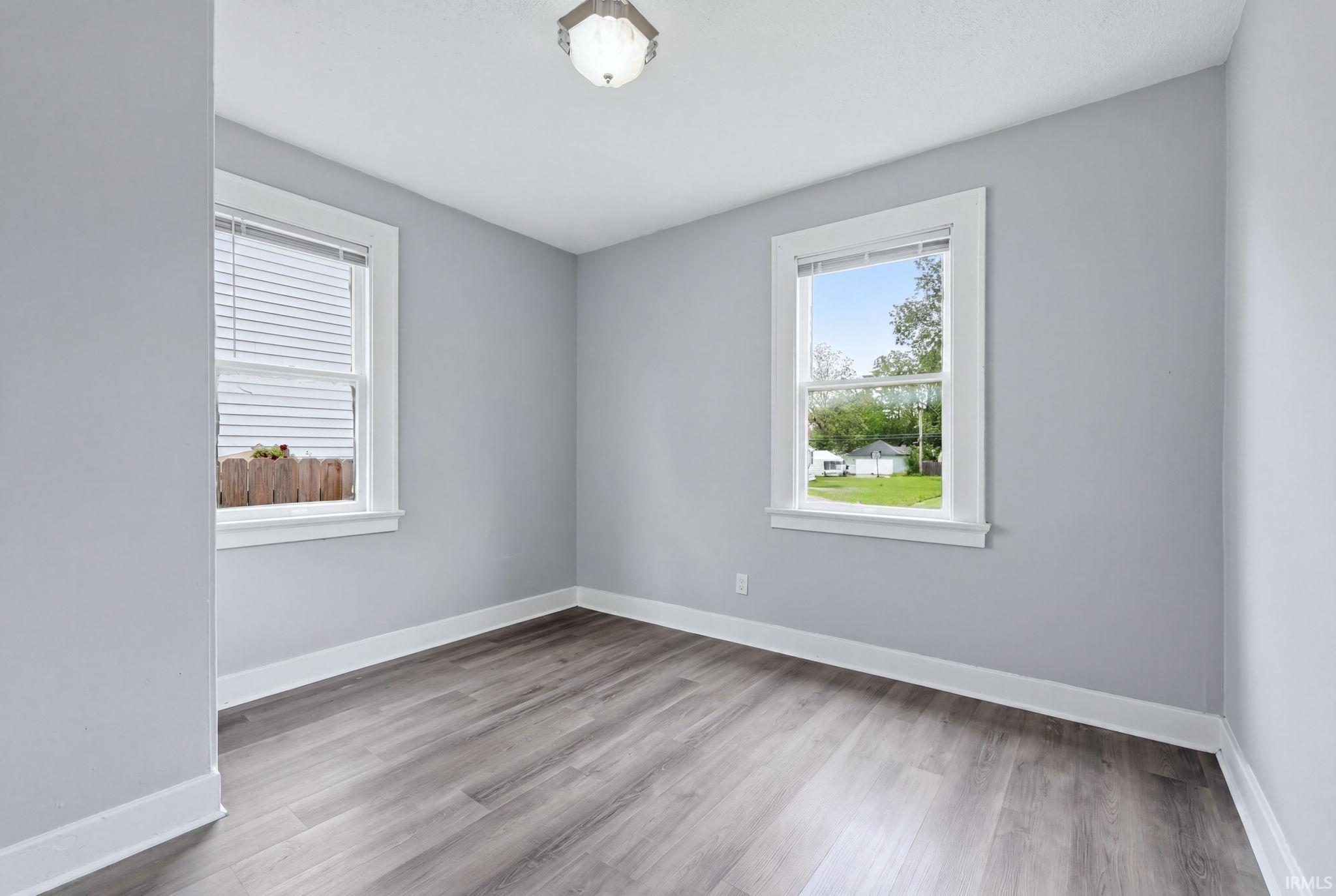 Light gray walls with white trim, wood-finish flooring, two double-hung windows, and a semi-flush mount ceiling light fixture