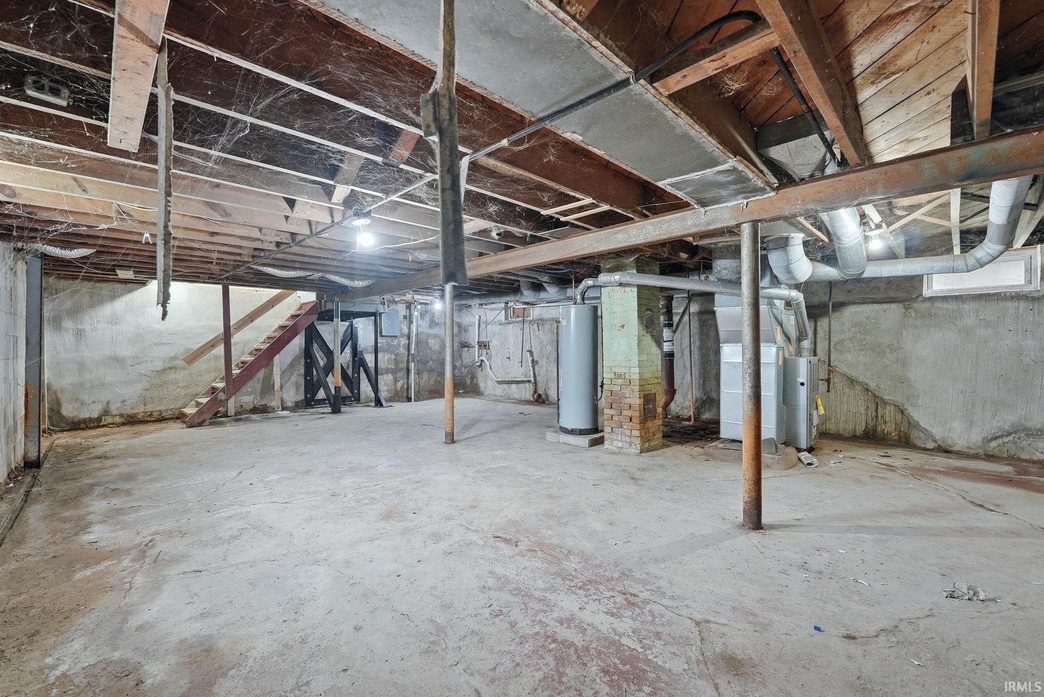 Unfinished basement featuring exposed wood joists, concrete flooring, and visible utility infrastructure including ductwork and water heaters