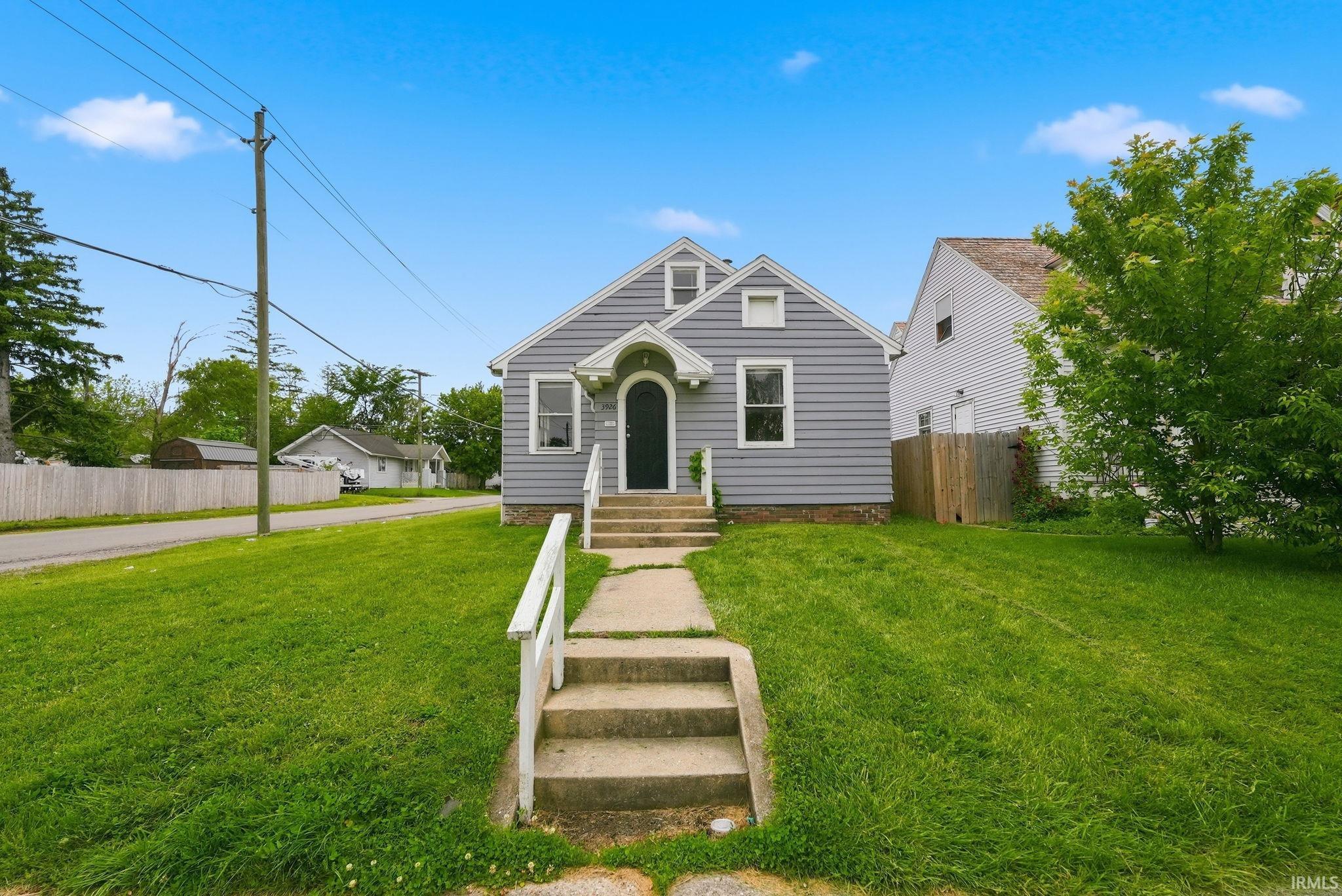 Cottage-style residence featuring light gray siding, a prominent arched entry, white framed windows, and concrete steps with white handrails
