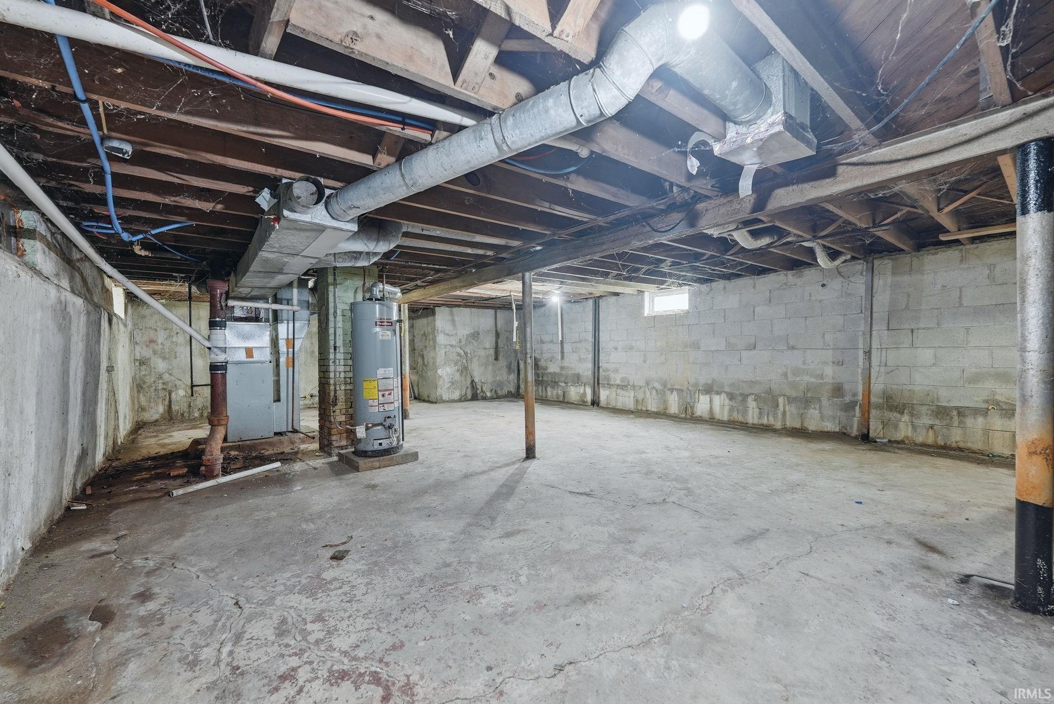 Unfinished basement featuring exposed wood joists, concrete block walls, a concrete floor, and utility systems including a water heater and furnace