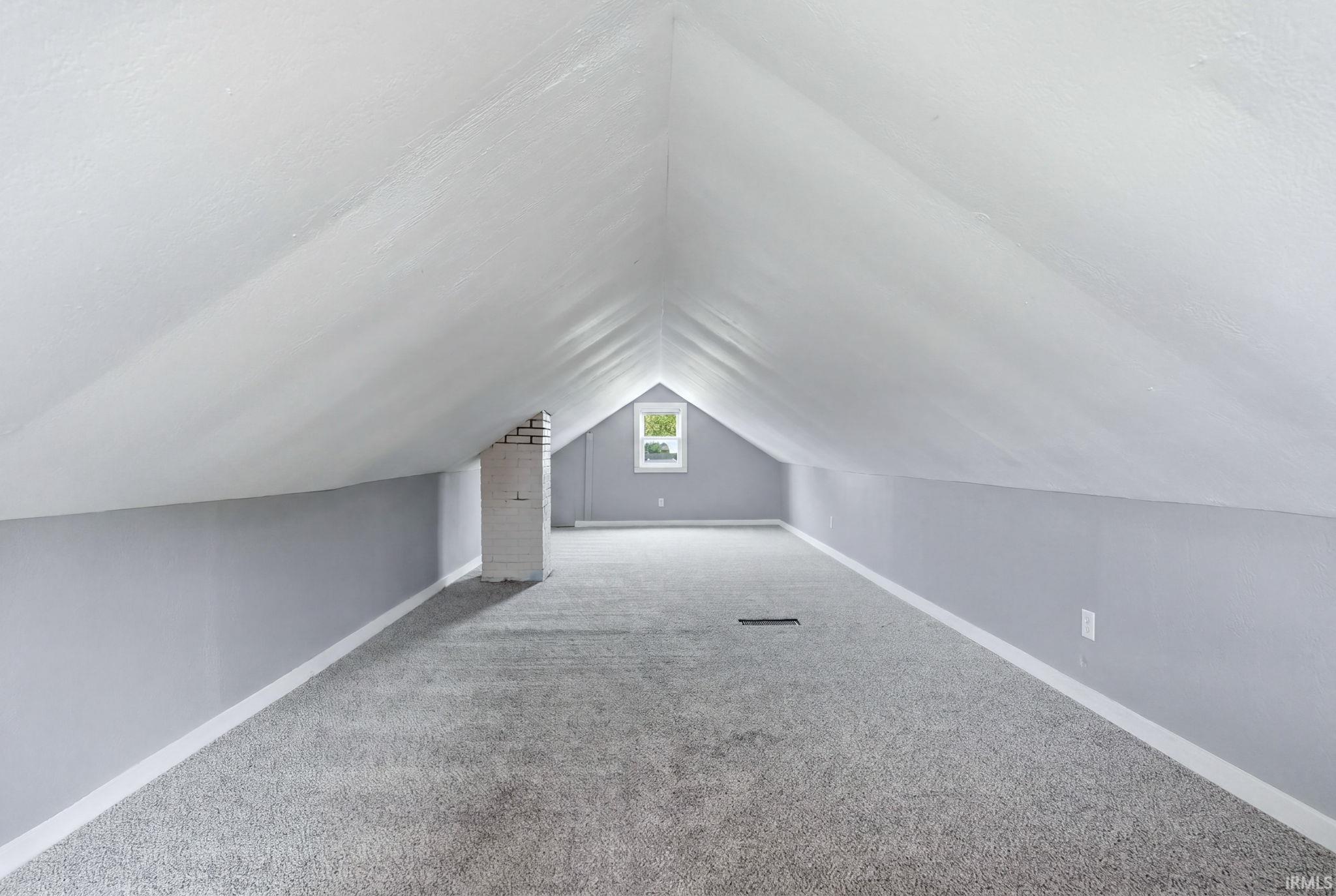 Spacious attic room featuring sloped white ceilings, gray wall panels, and gray carpeting