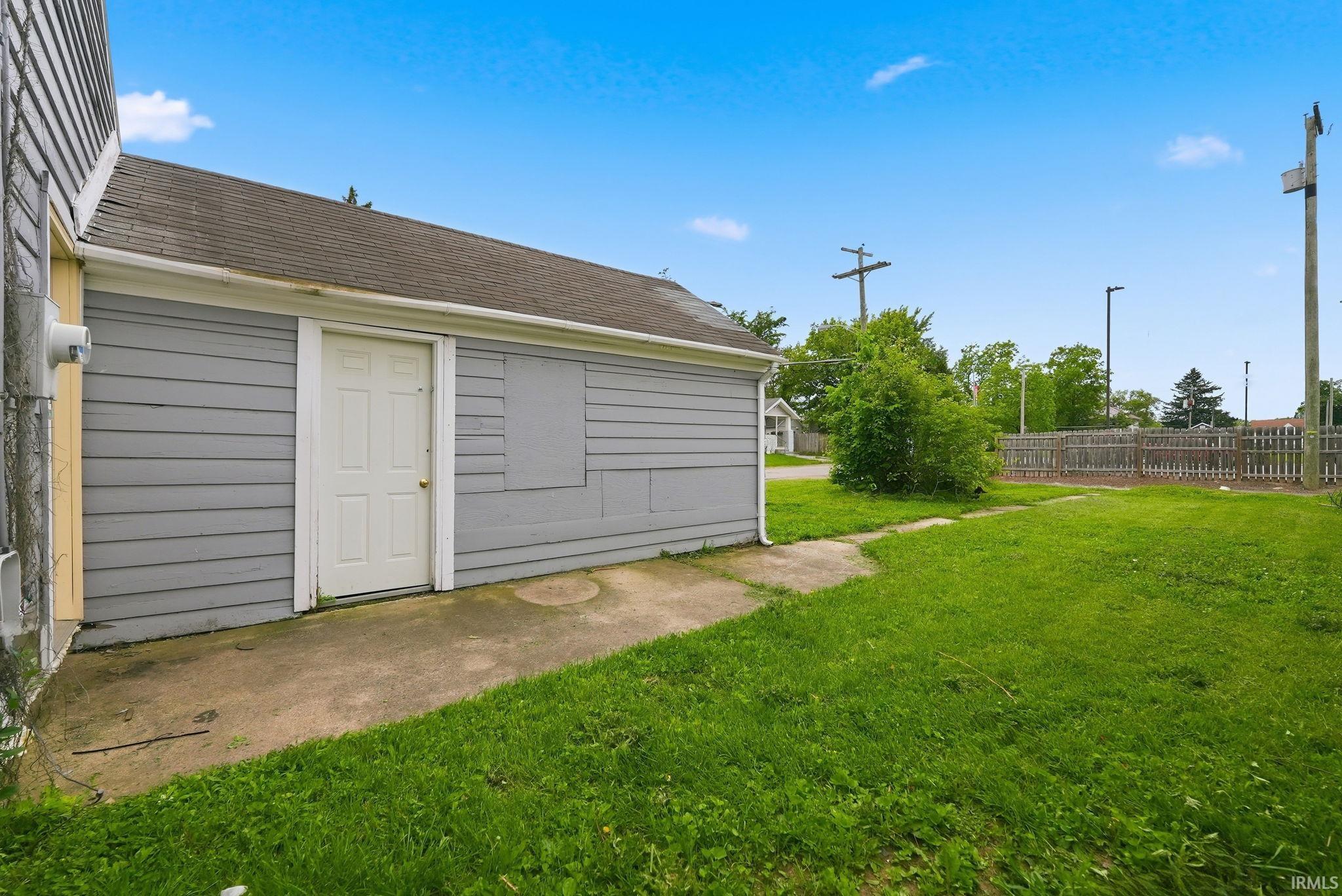 Attached garage structure with light gray horizontal siding, a white service door, and a shingle roof