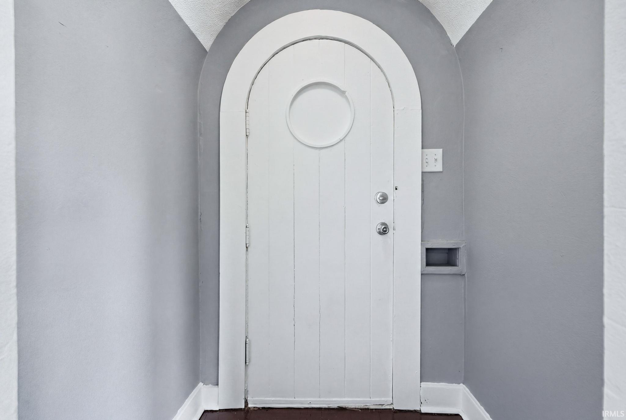 Arched doorway with a paneled white door, circular window accent, and dark wood-finish flooring