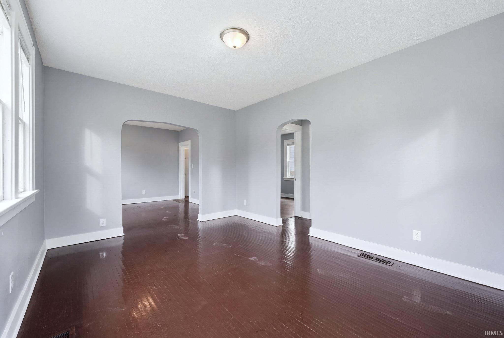 Spacious interior featuring a neutral color palette, wood-finish flooring, white trim, and arched doorways