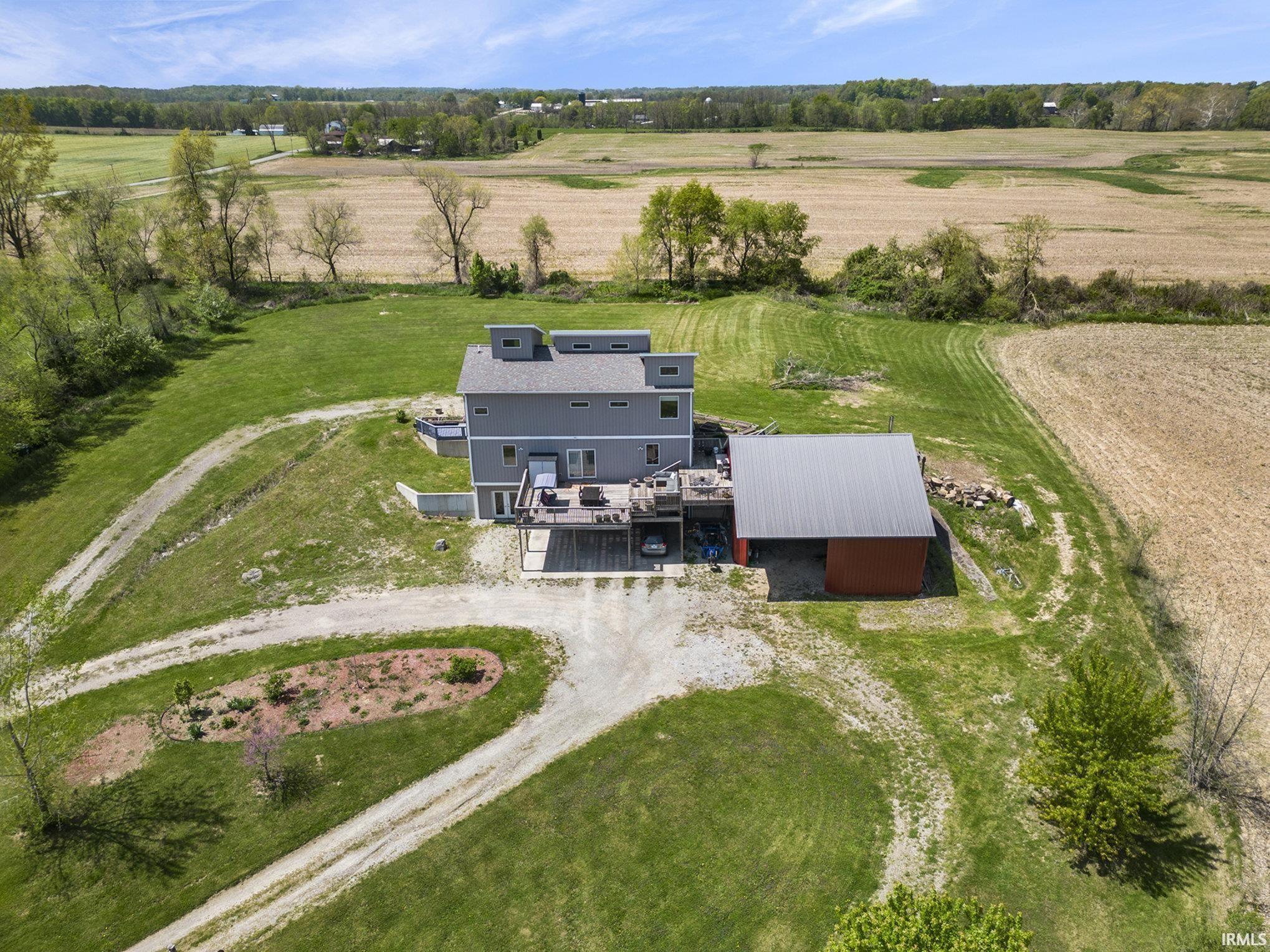 Modern-style residence with a multi-level deck, featuring a gravel driveway and surrounding green landscape