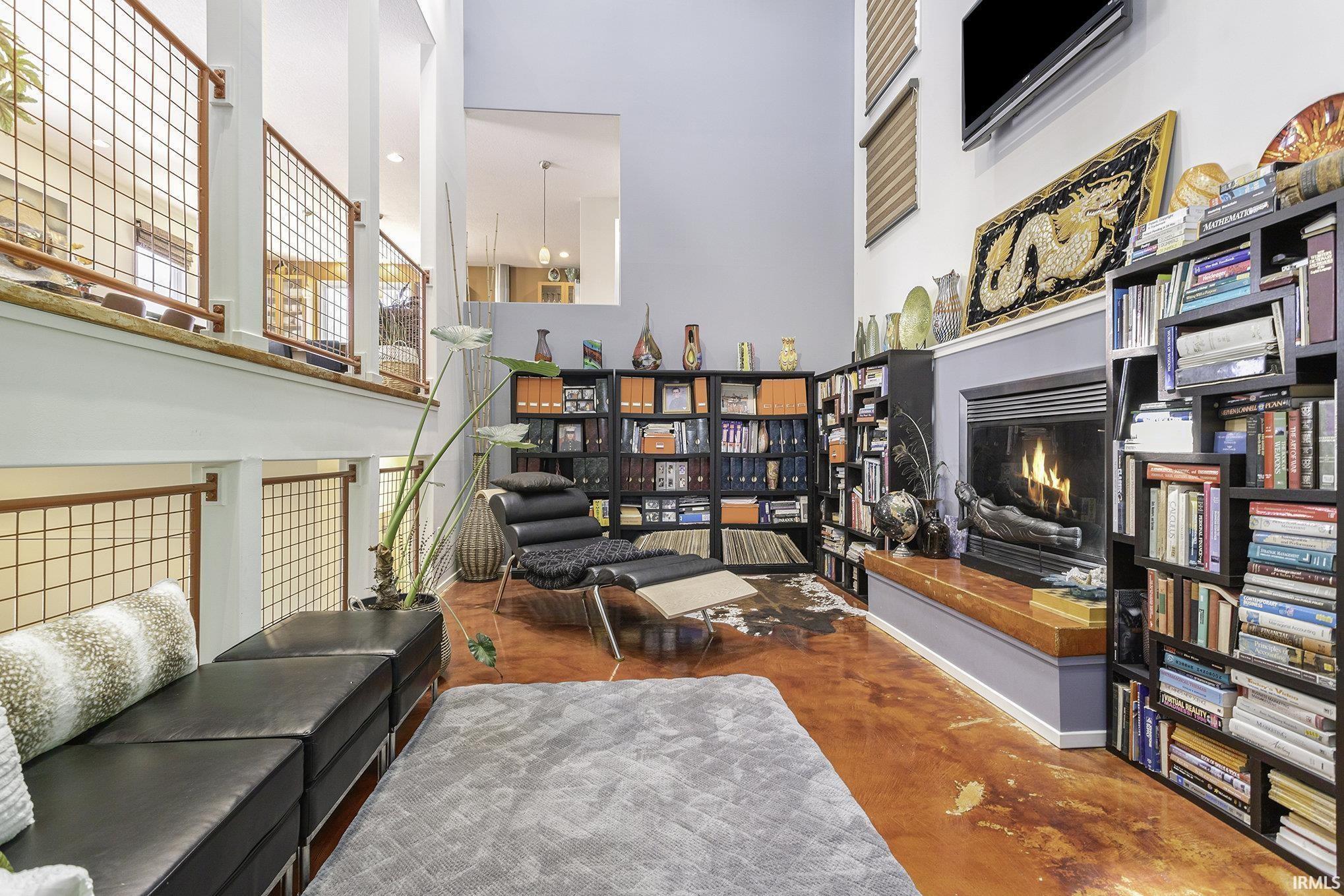 Two-story living area featuring a fireplace with a wood mantel, polished concrete flooring, a high ceiling, and an upper-level balcony with metal grid railings