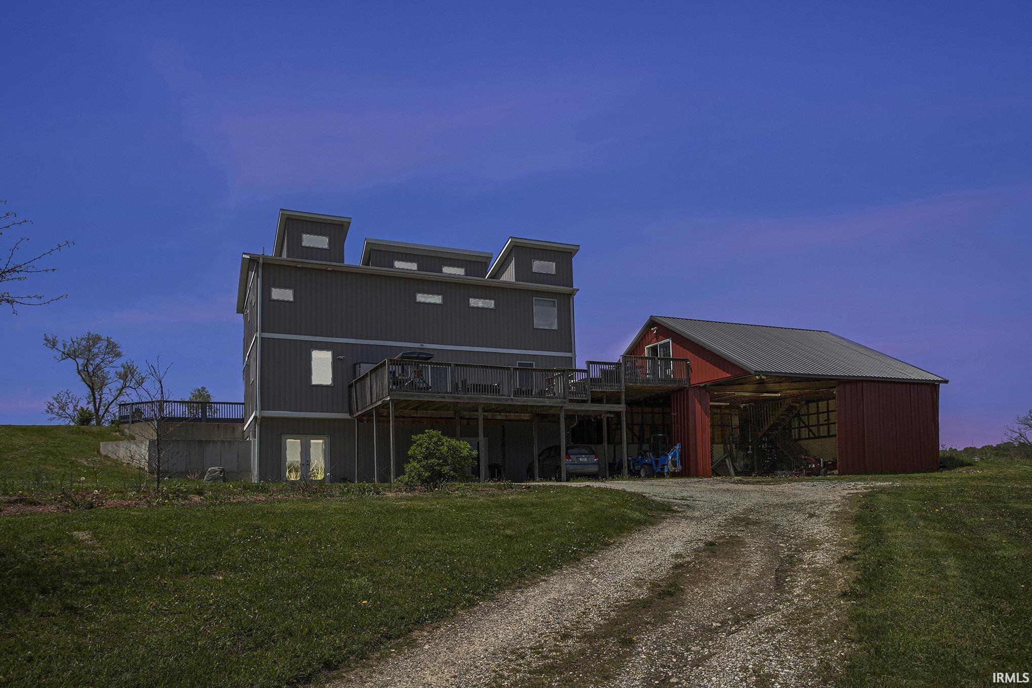 Contemporary residence with a dark gray exterior and multiple balconies, accompanied by a red barn featuring a metal roof and an upper-level deck