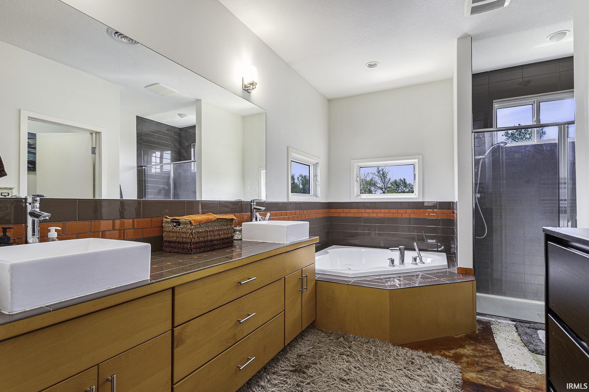 Bathroom featuring a dual vanity with rectangular vessel sinks, a jetted corner tub, and a separate shower with a glass enclosure