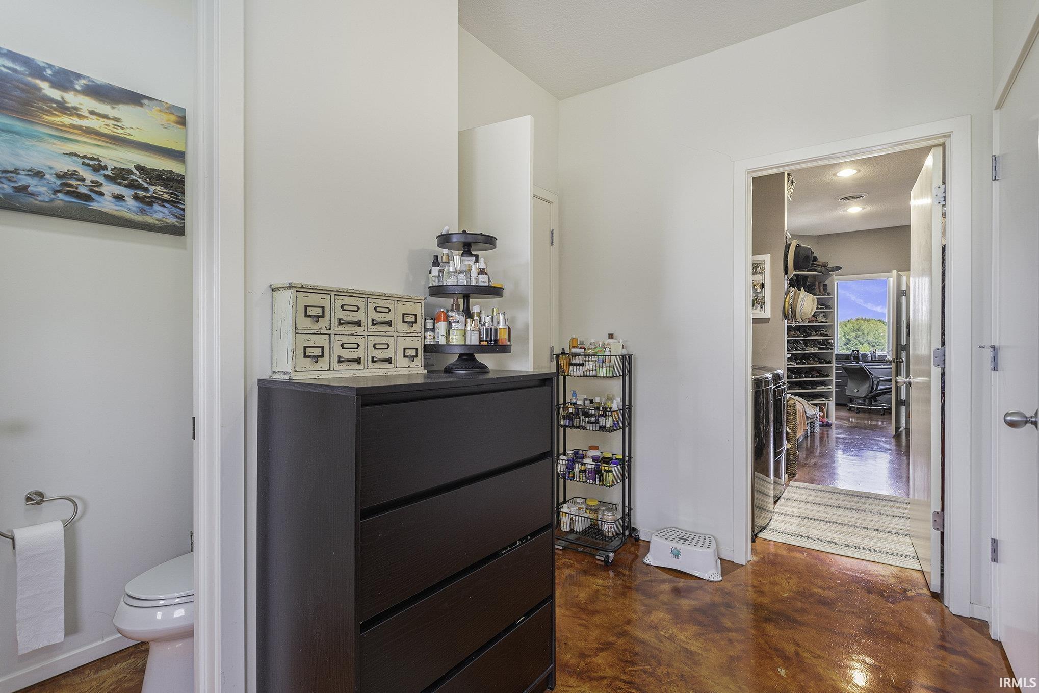 Polished concrete flooring extends through this interior hallway, featuring a powder room with a toilet and a doorway opening to an additional room