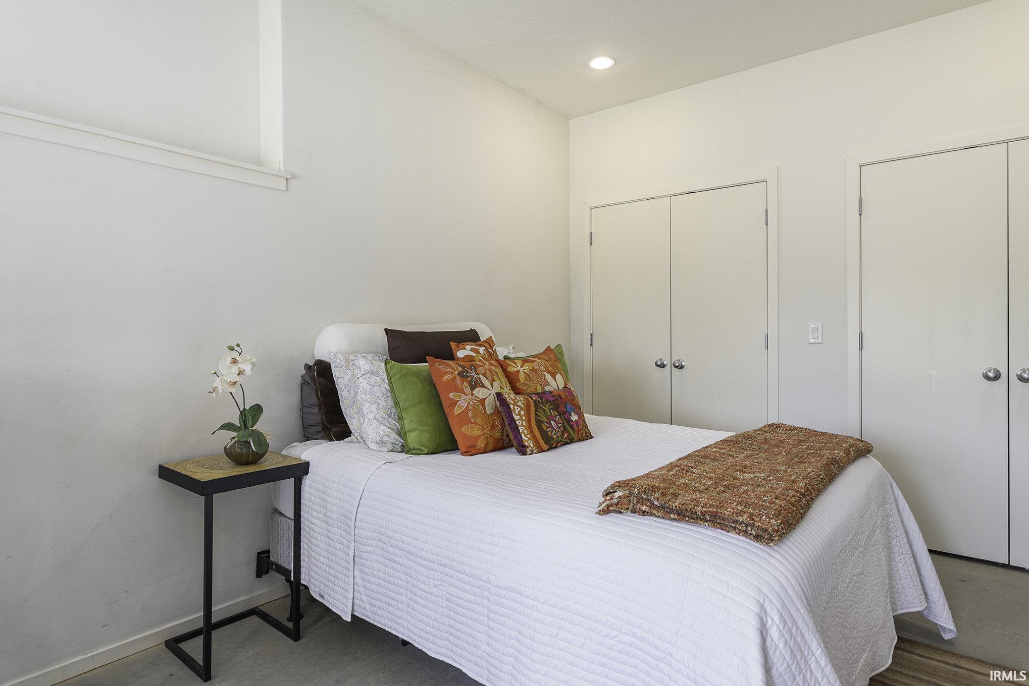 Spacious room featuring light-colored walls, built-in closet storage with bi-fold doors, recessed lighting, and a neutral flooring surface