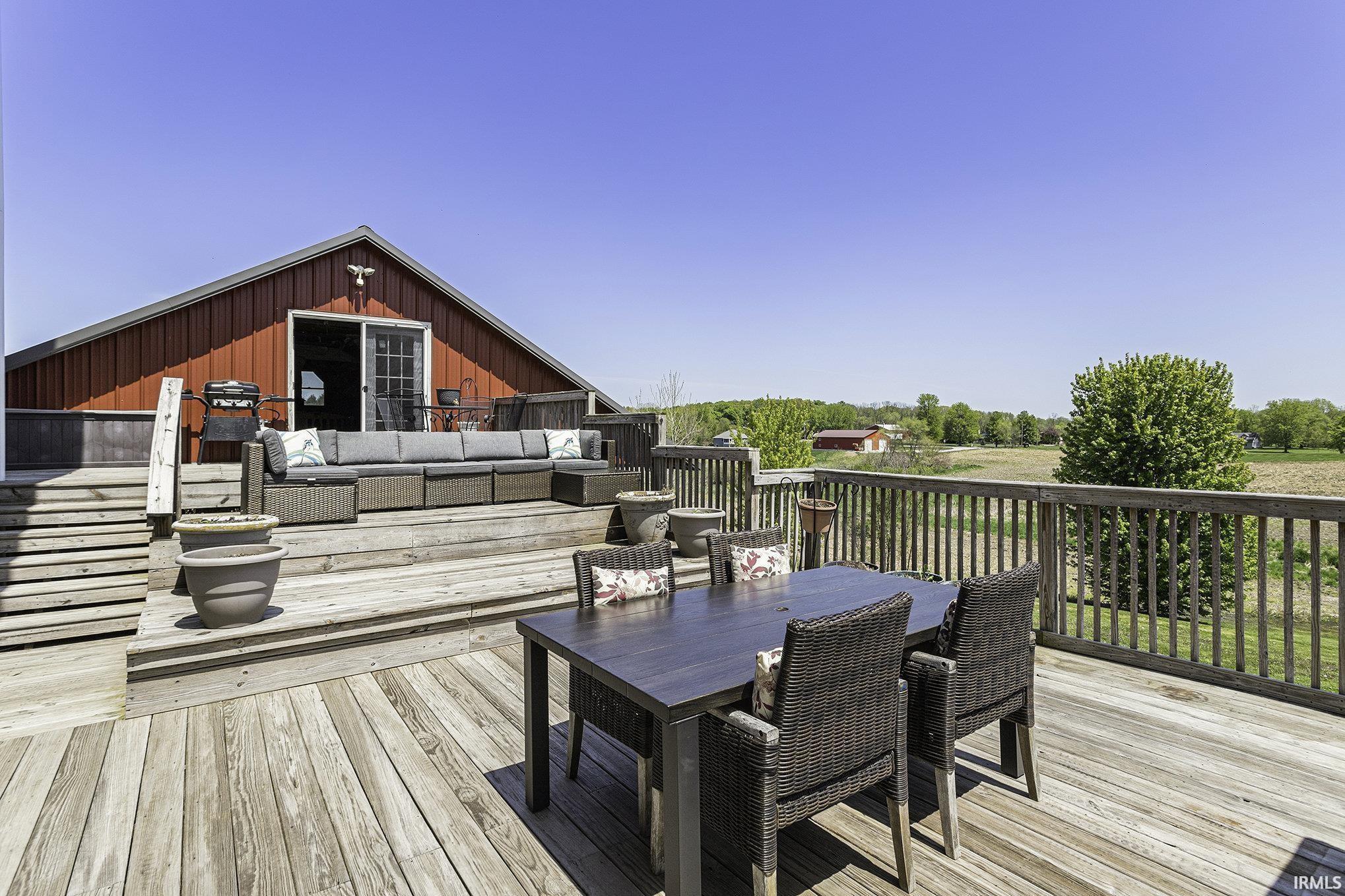 Multi-level wood deck featuring a barn-style structure with sliding glass doors, wooden railing, and open field scenery