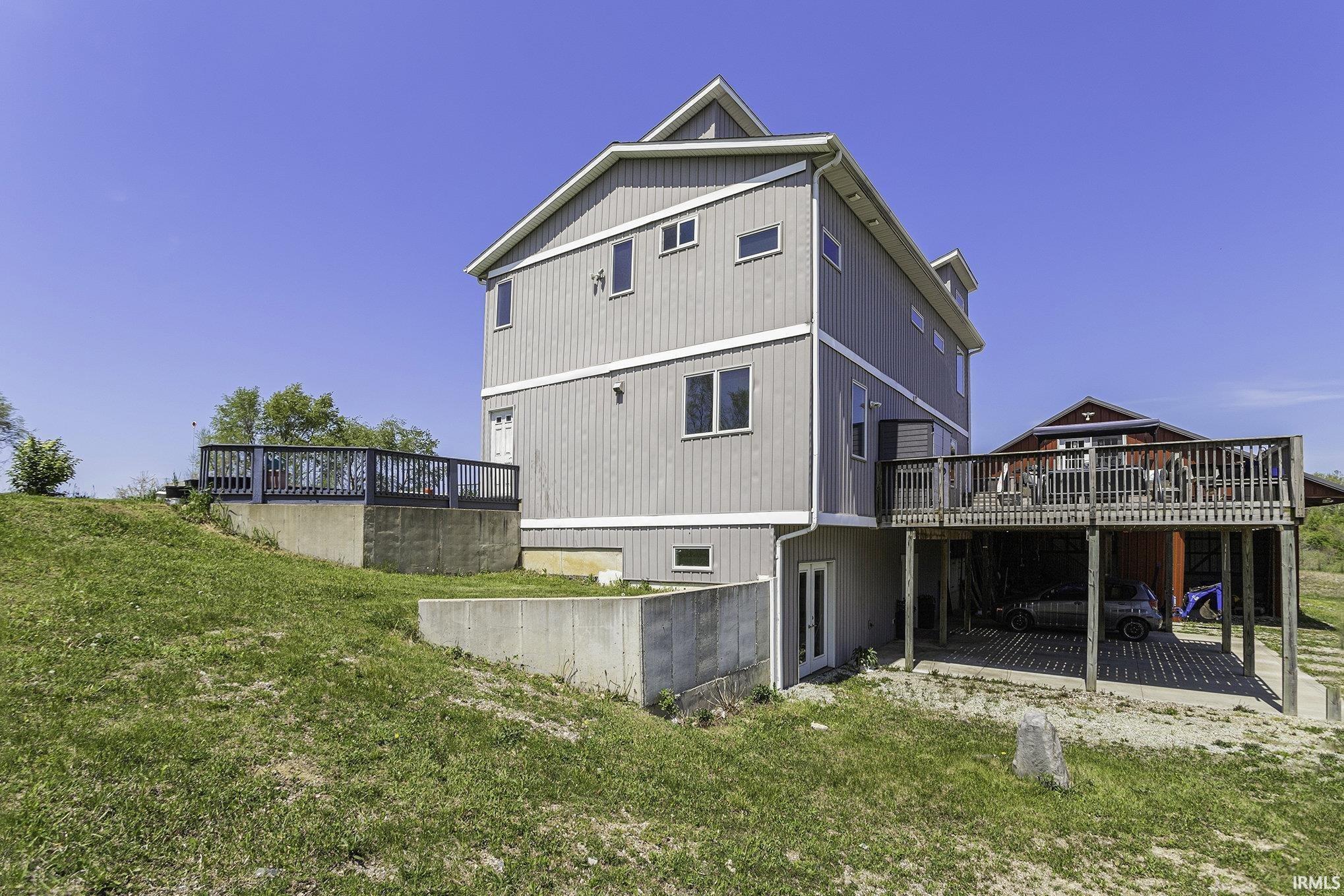 Multi-level gray-sided residence featuring two exterior decks with dark railings, a ground-level walkout entrance, and an integrated carport space