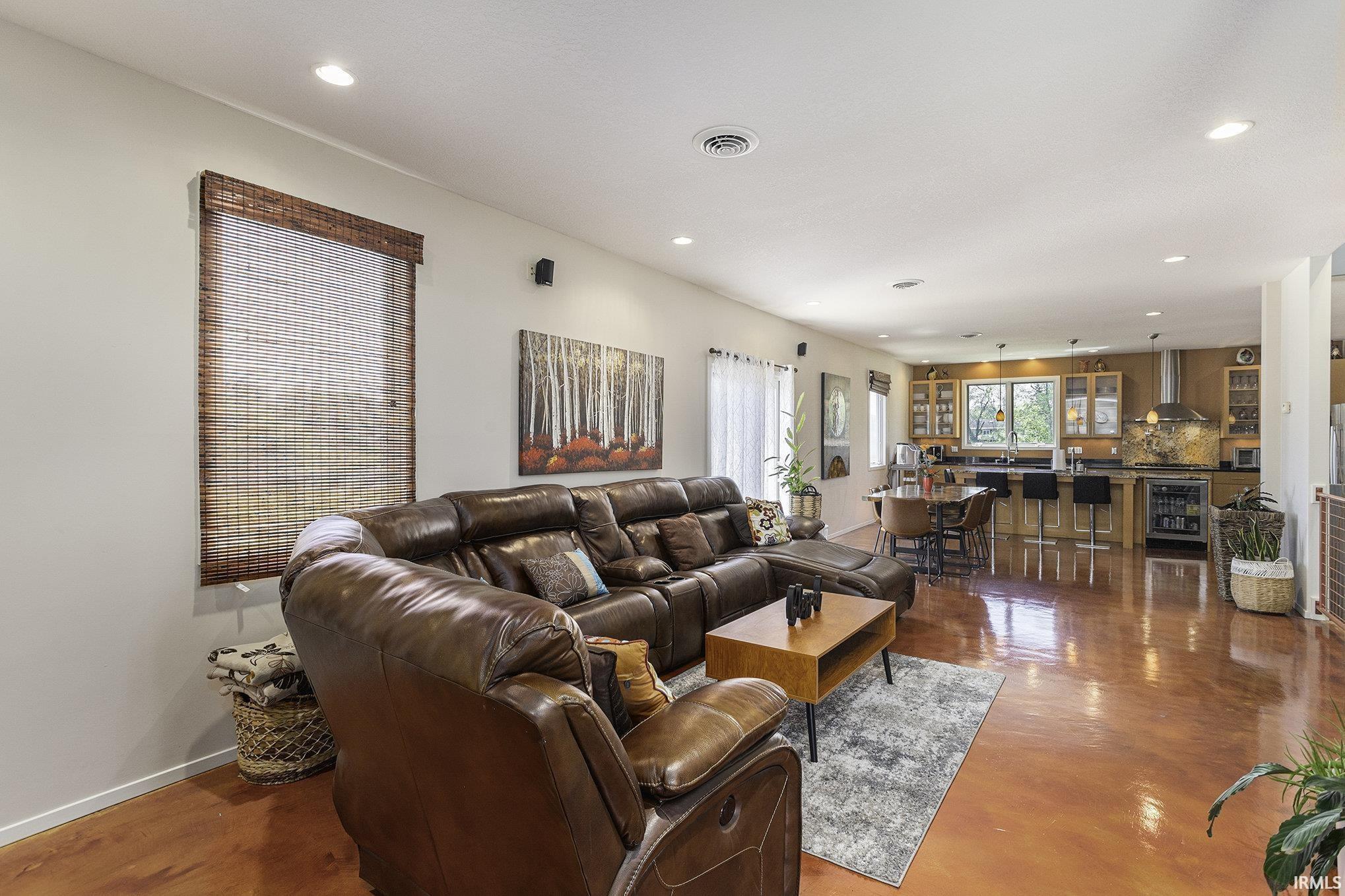 Open-concept living space featuring high ceilings with recessed lighting, wood-finish flooring, and multiple windows with woven blinds