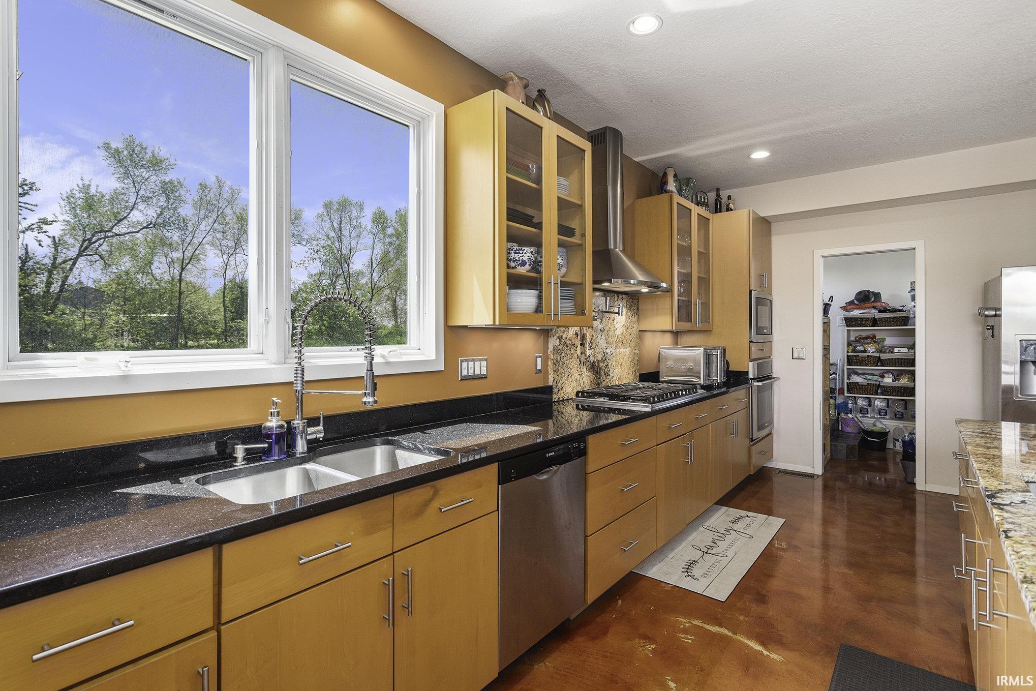 Kitchen featuring expansive windows, wood-finish cabinetry, black countertops, and stainless steel appliances