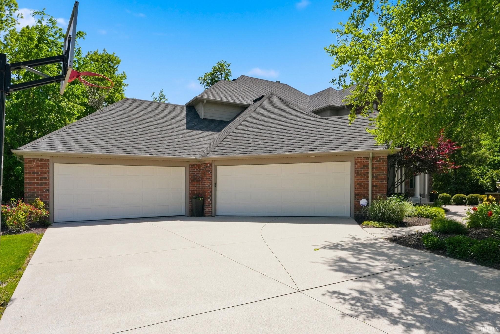 Brick-front residence featuring a two-stall garage, a concrete driveway, and mature landscaping