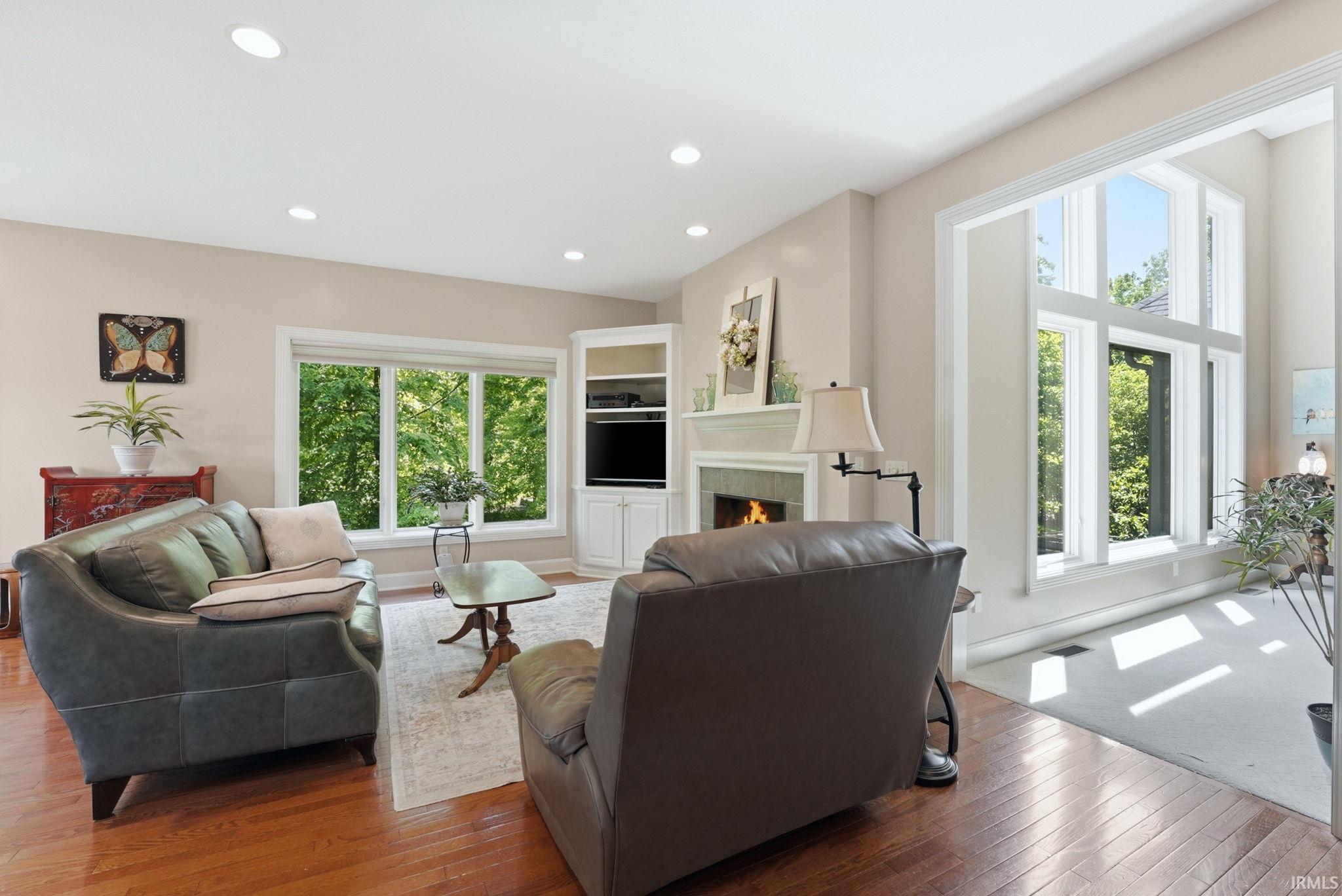 Living area featuring wood-finish flooring, recessed lighting, and a fireplace with a stone surround