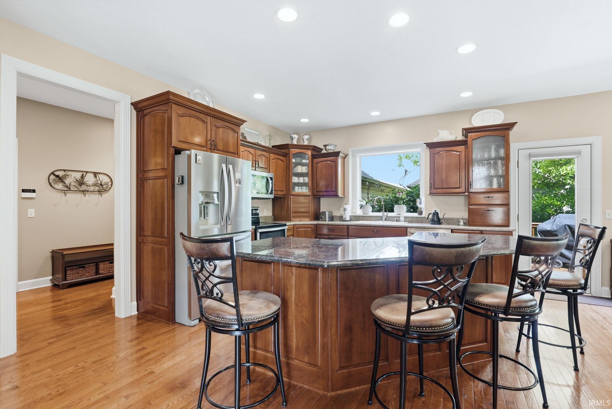 Spacious kitchen featuring hardwood flooring, recessed lighting, wood cabinetry, stone countertops, and a full suite of stainless steel appliances
