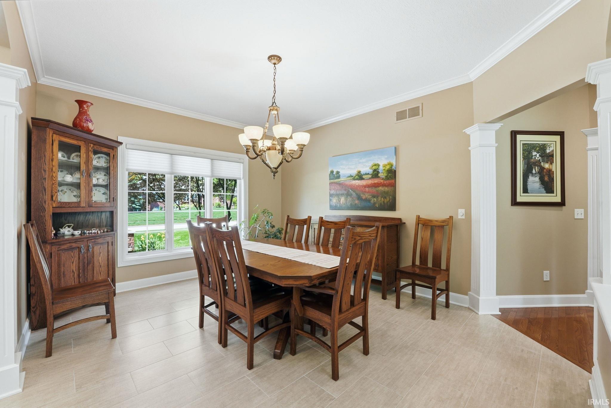 Formal dining space featuring light tile flooring, crown molding, a multi-pane window, and a decorative chandelier