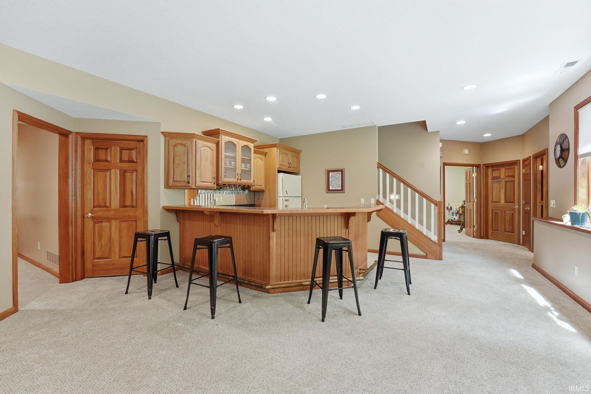 Built-in wooden wet bar with glass-front cabinetry, an integrated sink, and recessed lighting