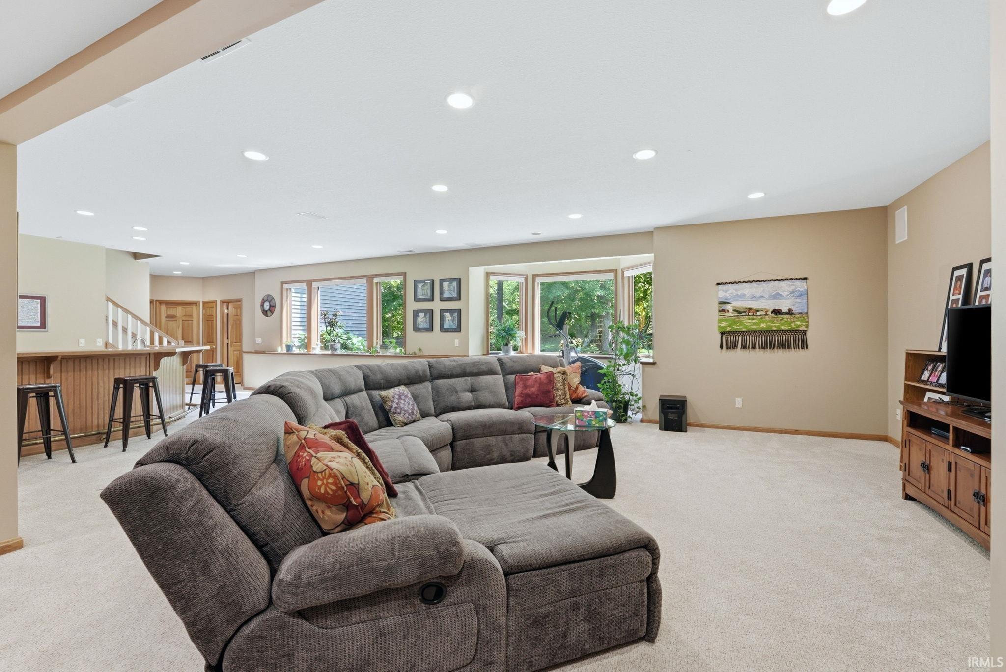 Spacious recreational area featuring recessed lighting, light-toned carpeting, a built-in wet bar with wood paneling, and multiple windows