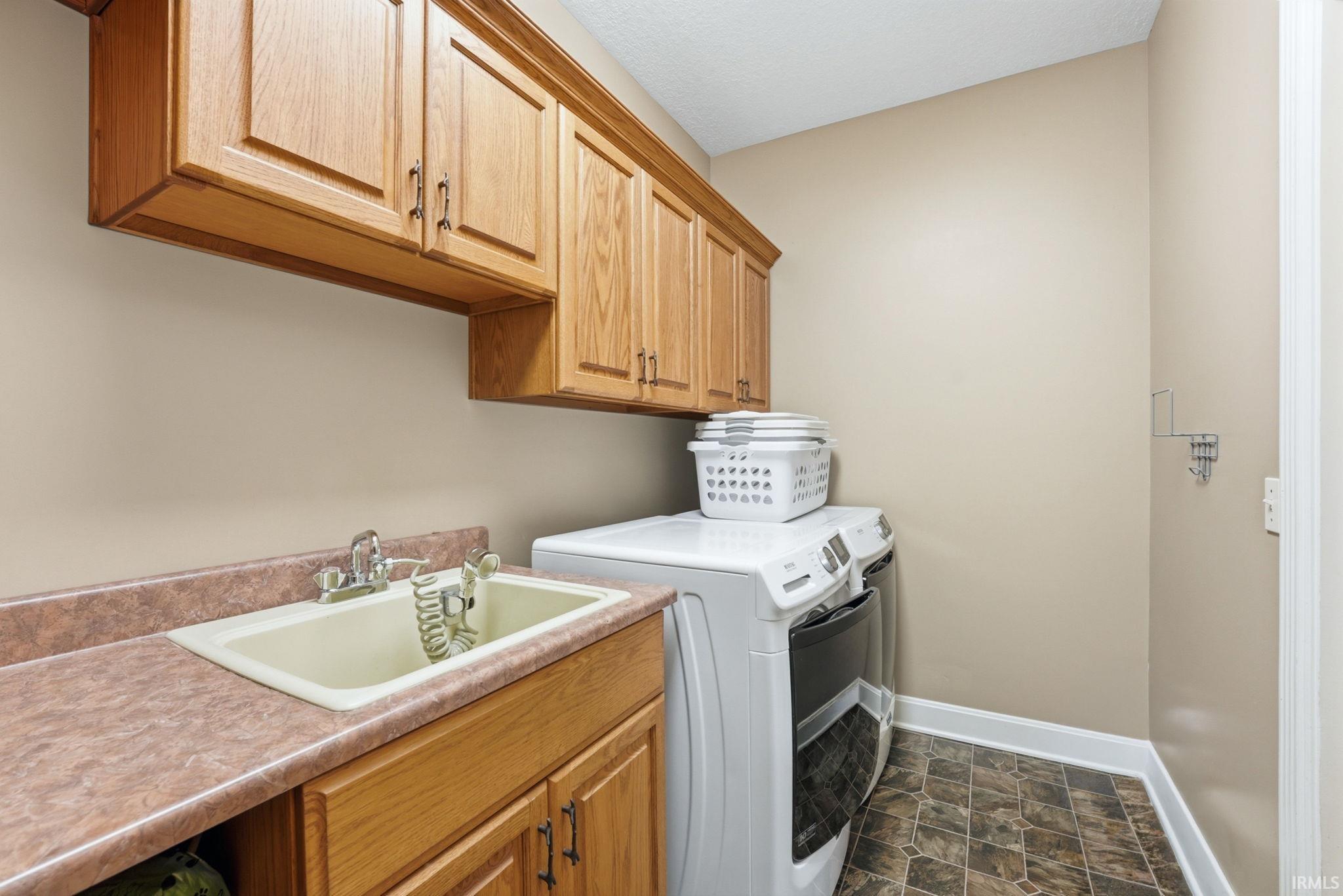 Laundry room featuring wood-finish cabinetry, a utility sink with dual faucets, and a patterned tile-look floor