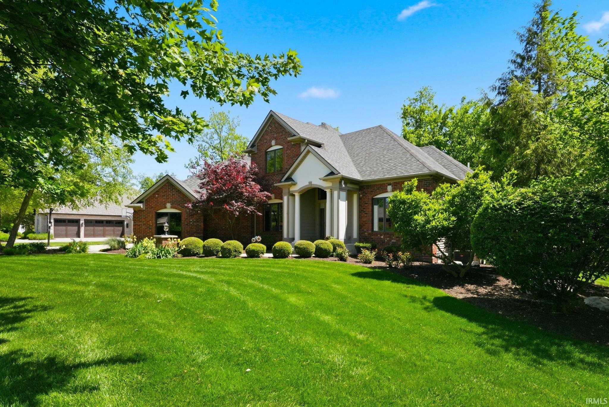 Brick exterior residence with a columned portico, a three-car garage, and mature landscaping