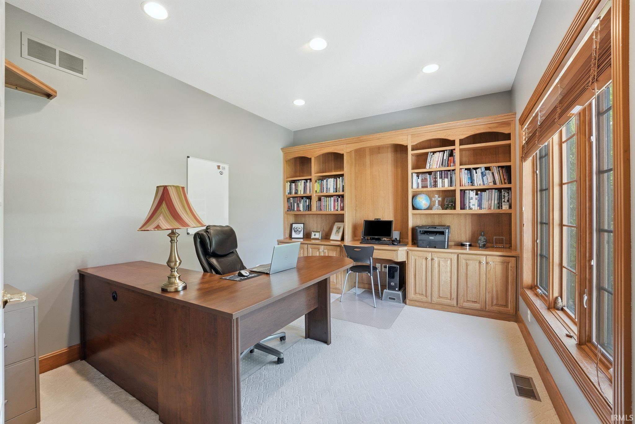 Dedicated room featuring a built-in wood-finish shelving unit, recessed lighting, expansive windows with wood-finish blinds, light-toned carpeting, and light gray wall paint