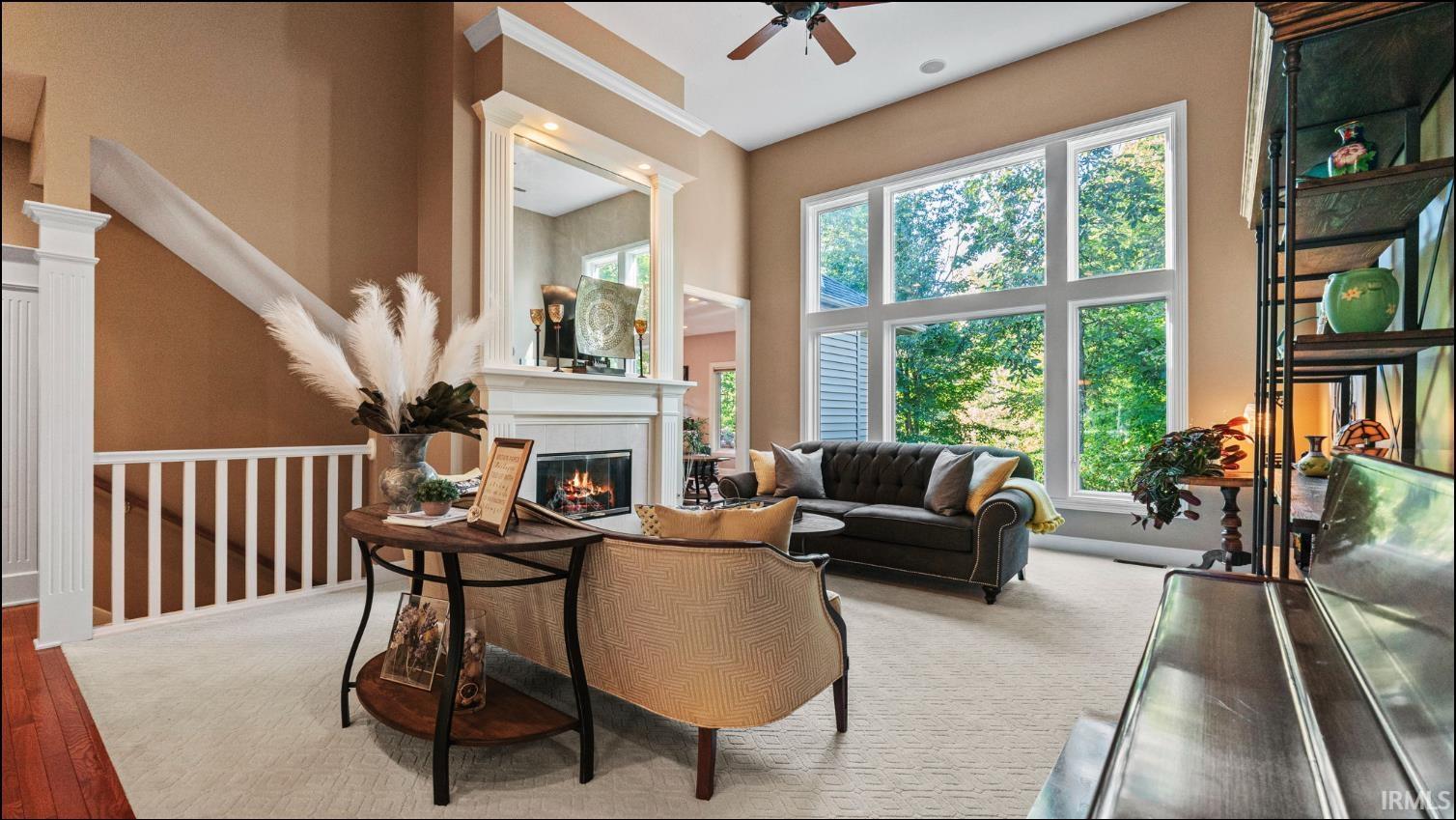 Spacious living area featuring a fireplace with a white mantel, tall windows, and a staircase with white balusters