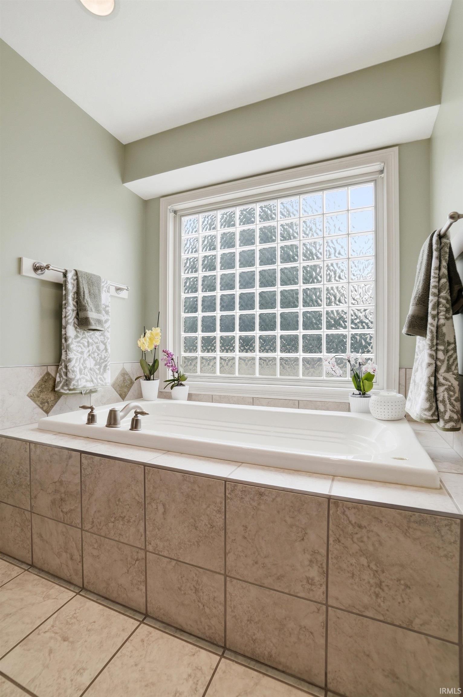 Built-in soaking tub with brushed nickel fixtures, surrounded by large format tile