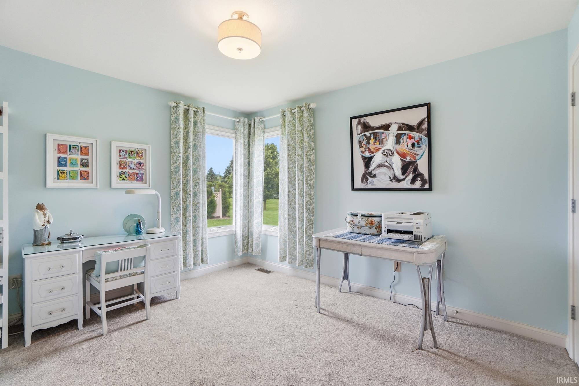 Bright room featuring light blue walls, neutral carpet flooring, and a large corner window providing natural light