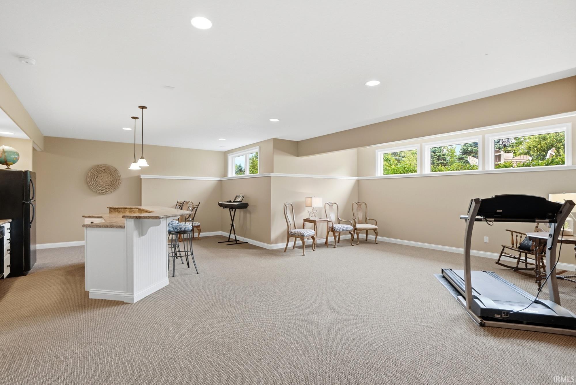 Spacious lower level featuring recessed lighting, a built-in bar with pendant lights, a light-toned carpet, and multiple windows providing natural light