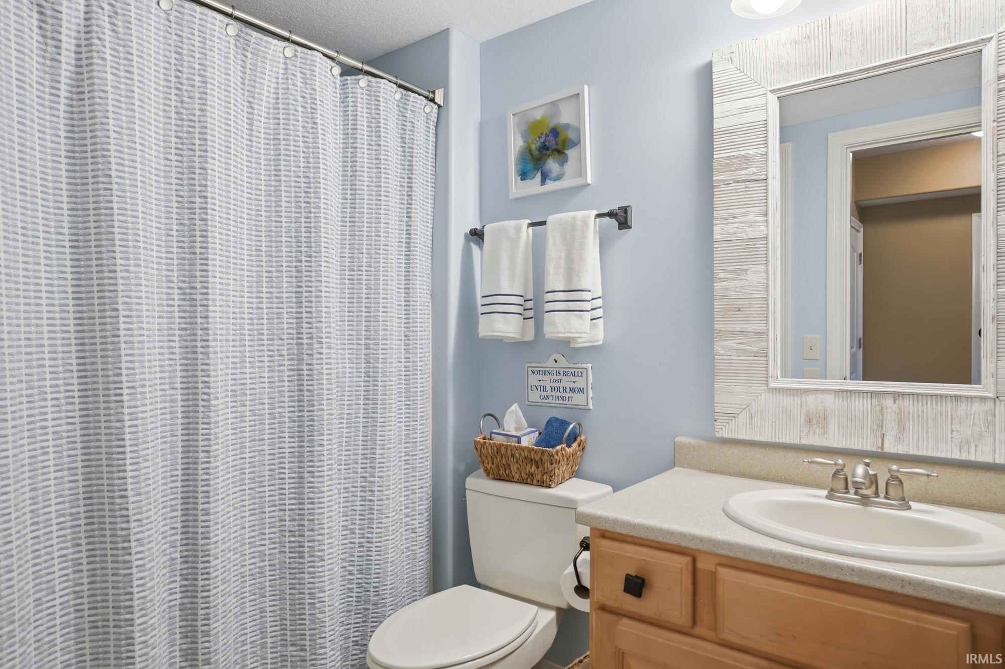 Bathroom featuring a white shower curtain, light blue wall paint, a vanity with a light-colored countertop, and a mirror with a wood-finish frame