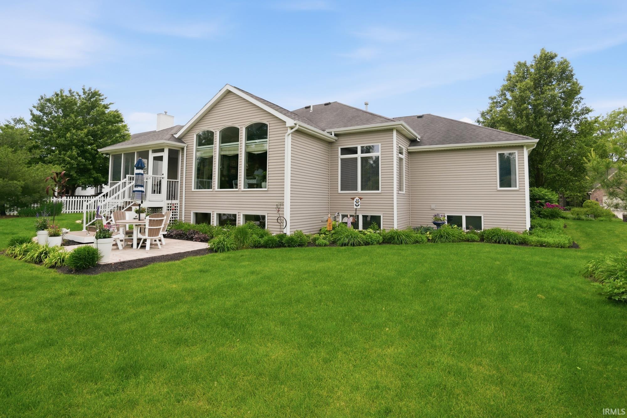 Expansive green lawn surrounds the property, featuring a ground-level patio with a screened porch overhead