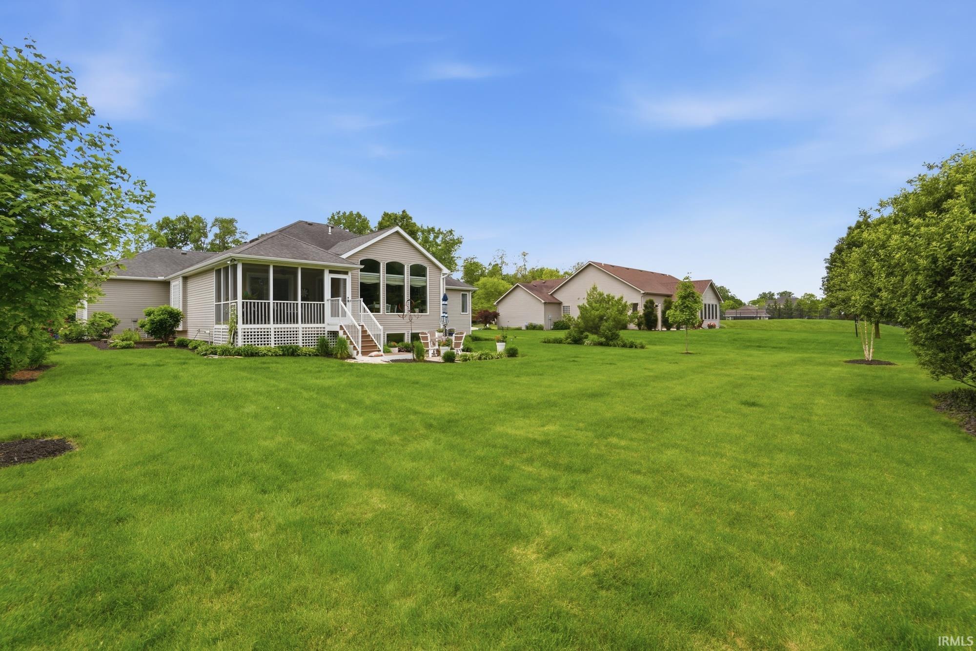 Expansive rear yard featuring a manicured lawn, mature trees, and landscaping