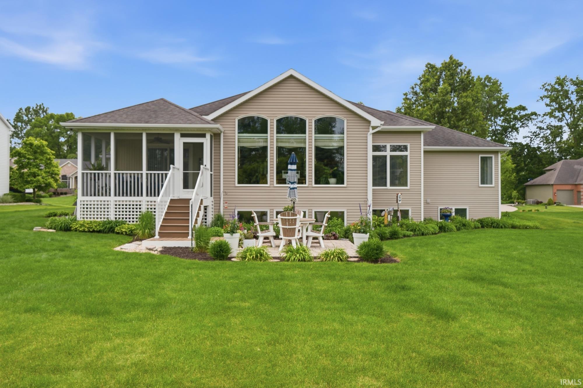 Rear exterior featuring a screened-in porch with white railing, a stone patio, and expansive lawn