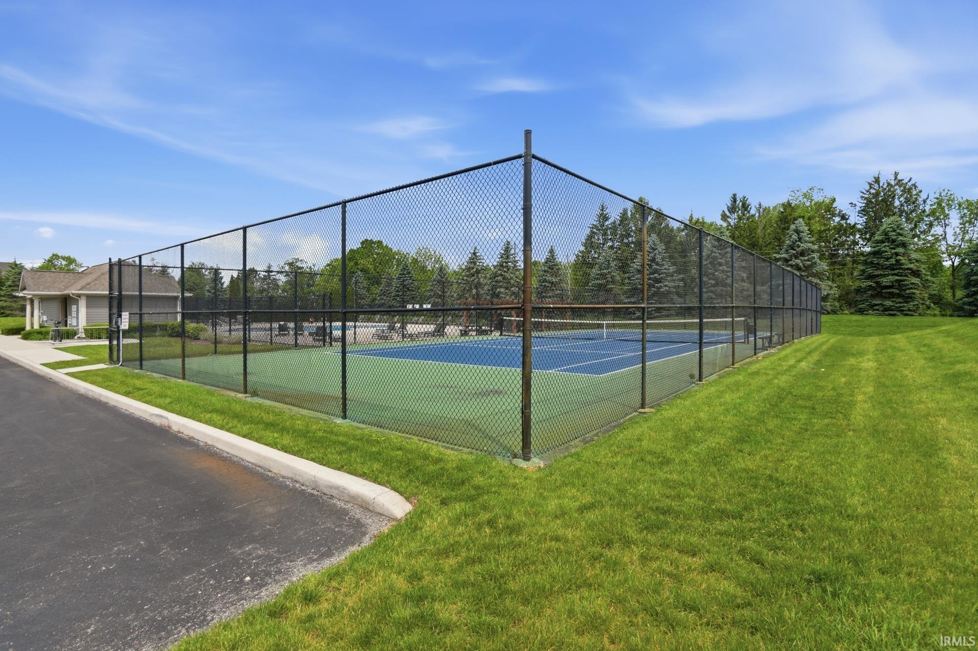 Outdoor tennis court with a blue and green playing surface, enclosed by a black chain-link fence