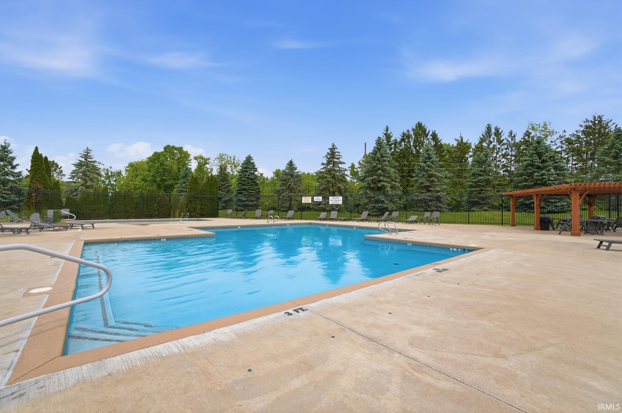 Outdoor swimming pool with concrete decking, a wooden pergola, and perimeter fencing
