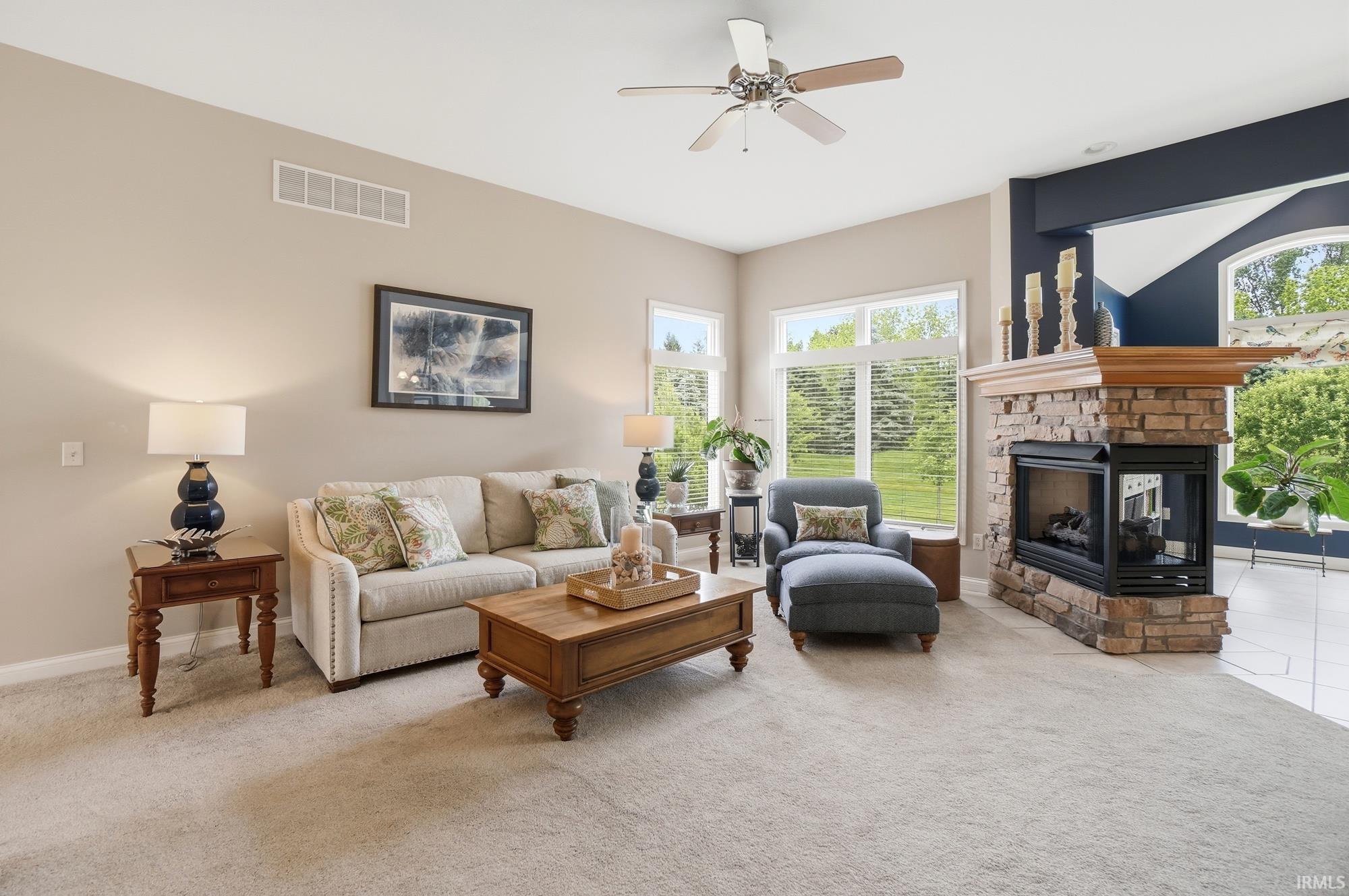 Living area featuring a stone-clad fireplace with a wood mantel, vaulted ceilings, and a ceiling fan
