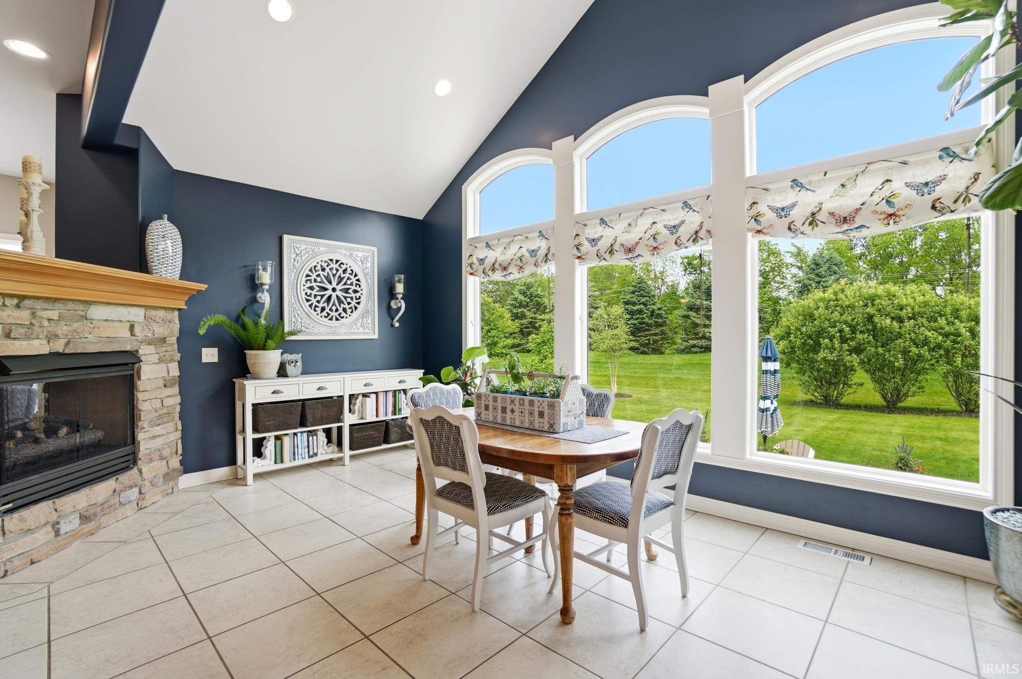 Vaulted ceiling space featuring a stone fireplace with a wood-finish mantel, built-in shelving, expansive arched windows, and tile flooring