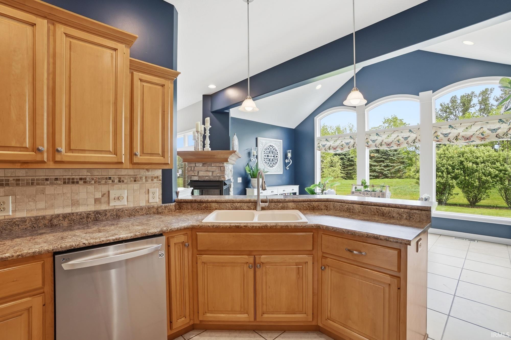 Kitchen featuring light wood cabinetry, a built-in double sink, stainless steel dishwasher, and a stone-look countertop with a tile backsplash