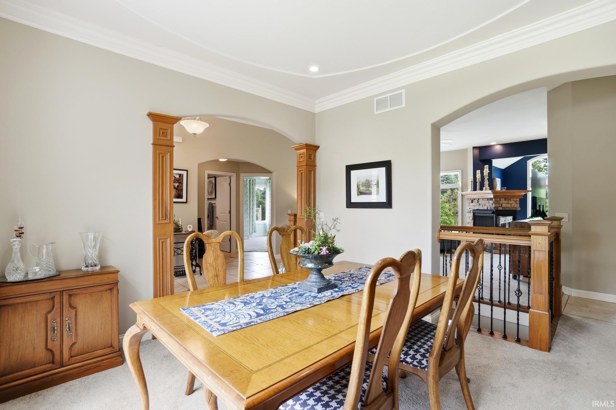 Formal dining area featuring an arched doorway with wood-framed pilasters, tray ceiling with crown molding, and neutral wall tones