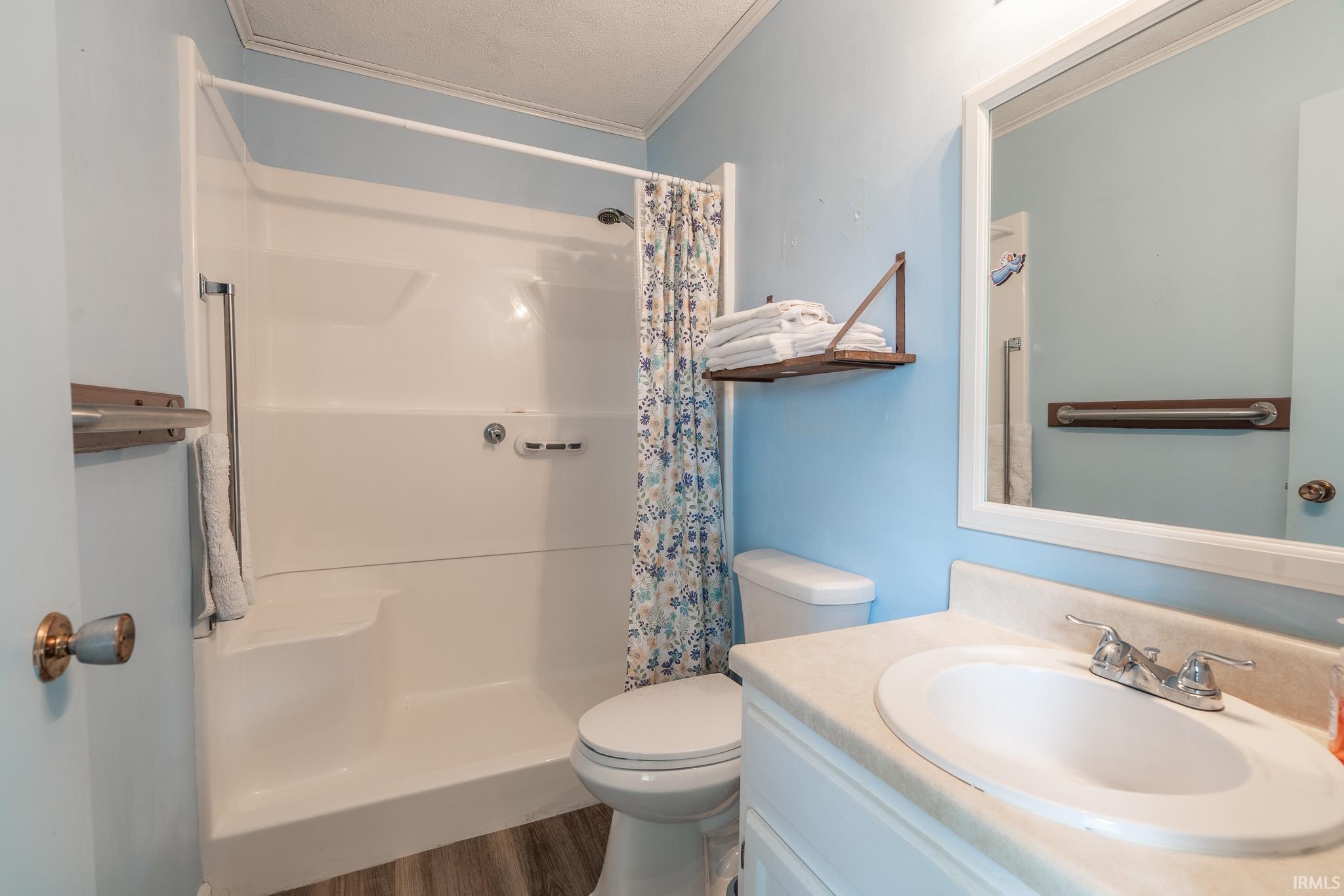 Bathroom featuring a white vanity with an integrated sink, a rectangular framed mirror, a white toilet, and a stand-up shower with an integrated bench