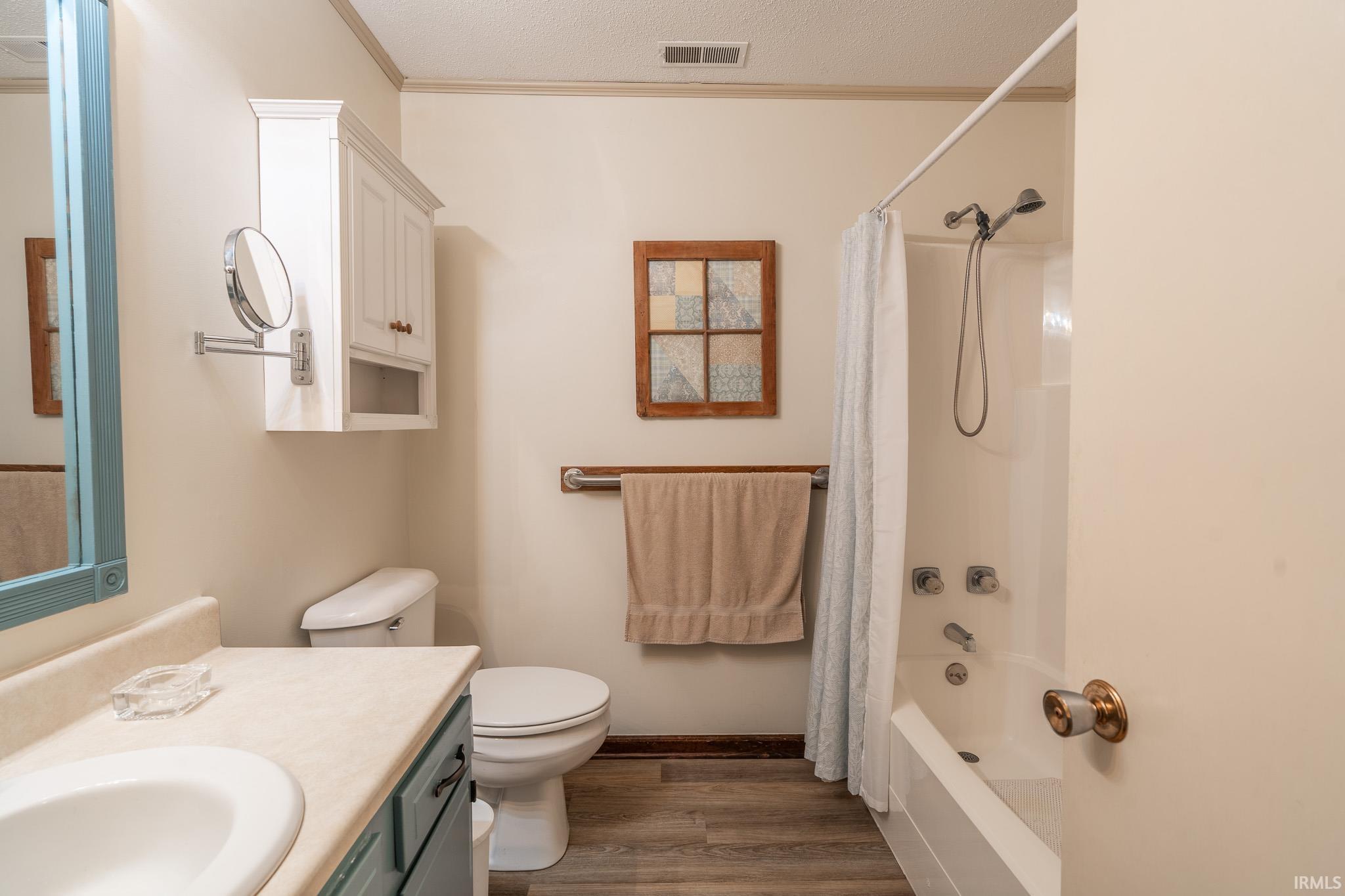Bathroom featuring a vanity with an integrated sink, white cabinetry, wood-finish flooring, a toilet, and a shower/tub combination with a wall-mounted showerhead