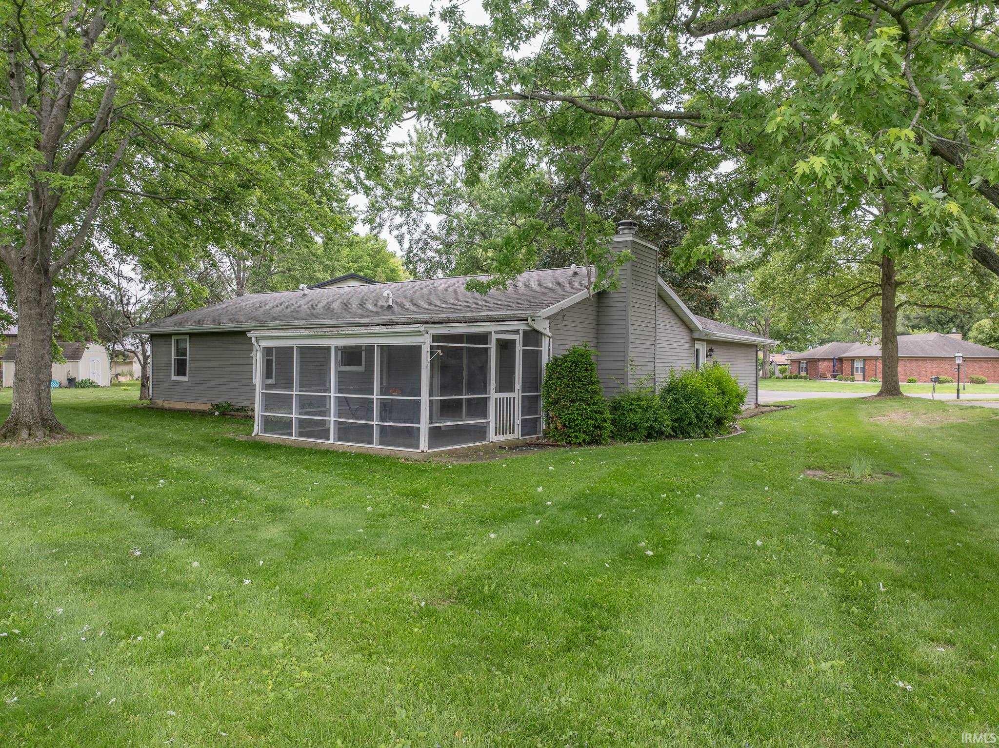 Expansive green lawn surrounds a single-story residence with gray siding and a screened porch