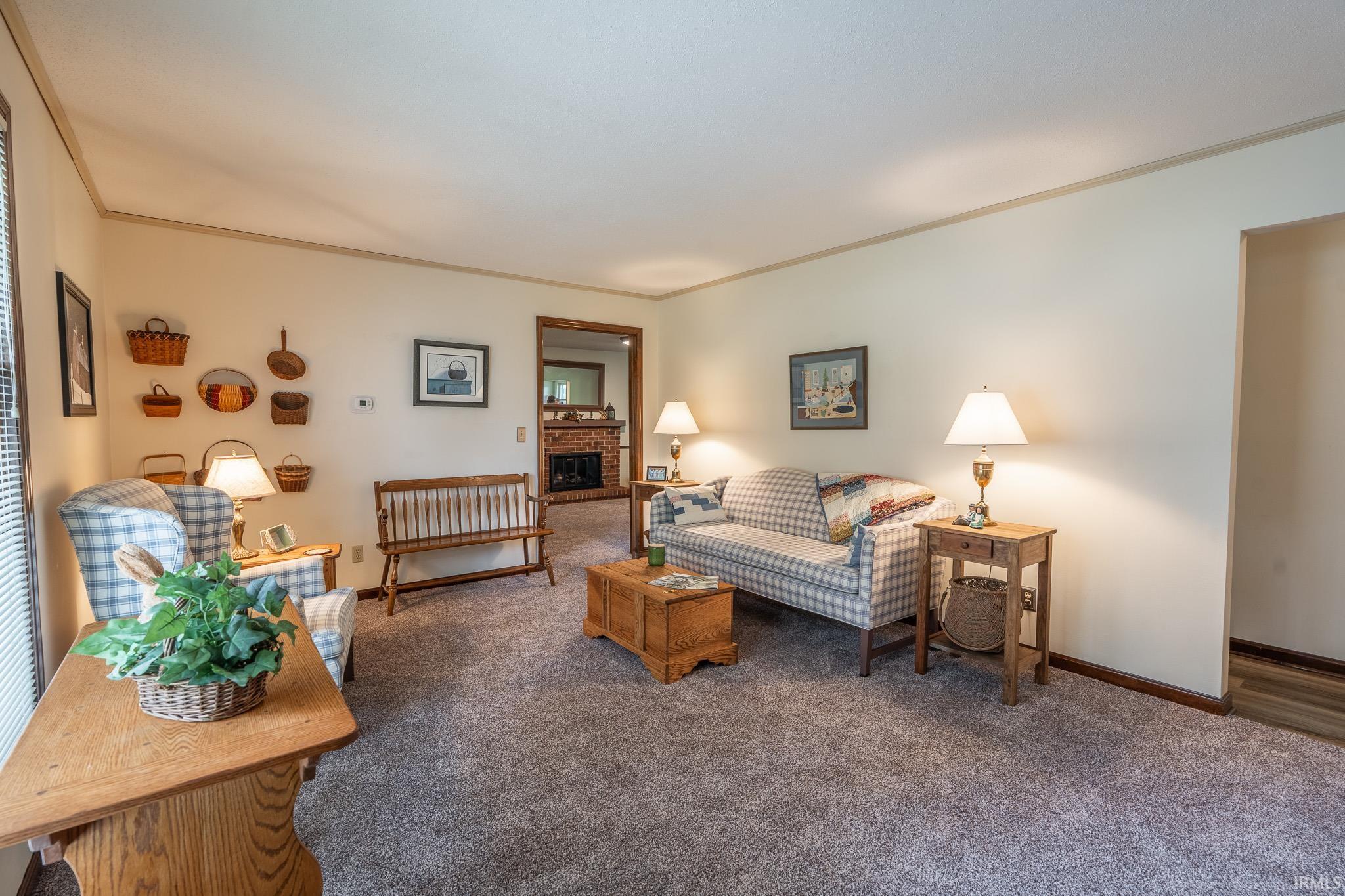 Carpeted living area featuring light-toned walls, wood trim accents, and an arched doorway leading to a brick fireplace
