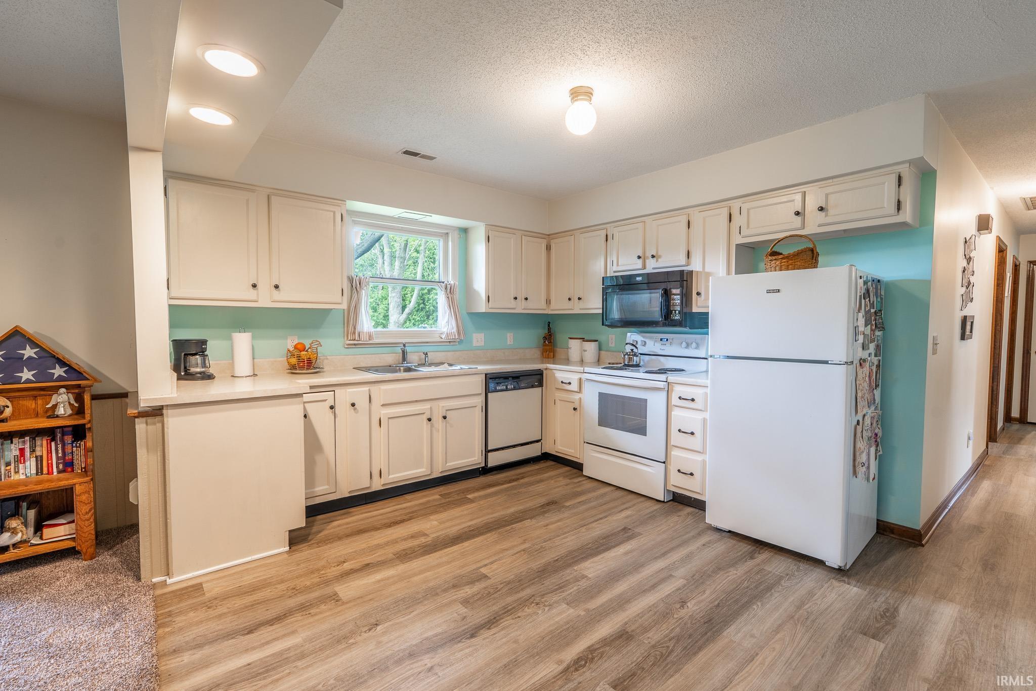 Kitchen featuring wood-finish flooring, white cabinetry, a window over the sink, recessed lighting, and a full suite of white appliances