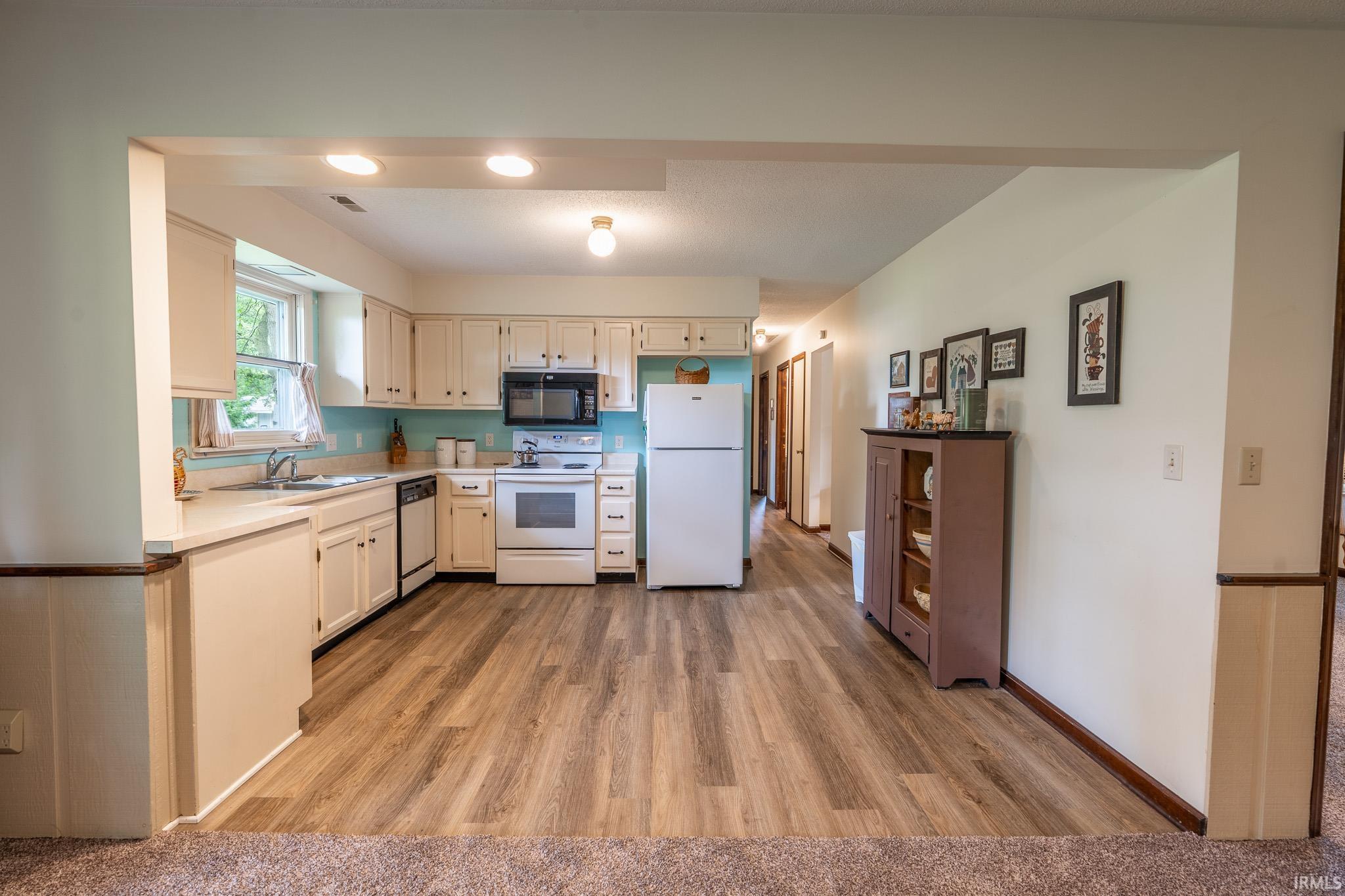 Kitchen featuring white cabinetry, light-toned countertops, a full suite of white appliances, recessed lighting, and wood-finish flooring